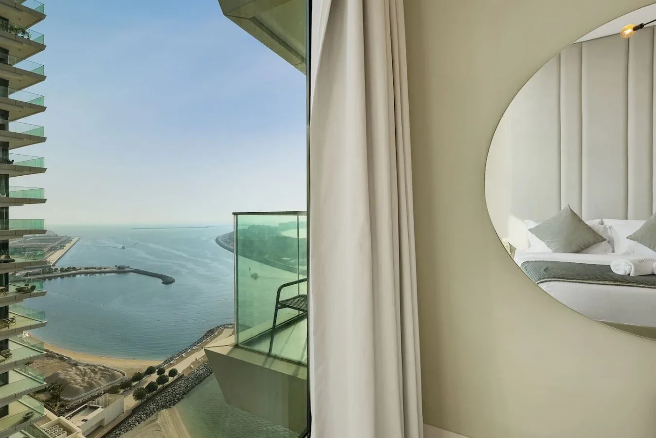 Un dormitorio con un espejo redondo junto a un balcón con vistas al agua.