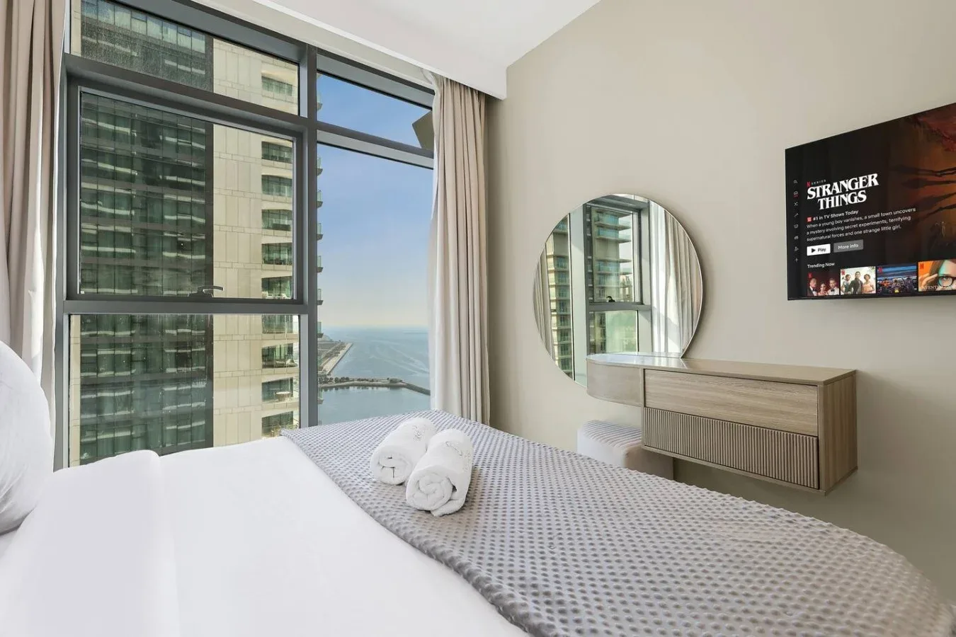 Un dormitorio con una gran ventana con vistas a edificios cercanos y al agua.