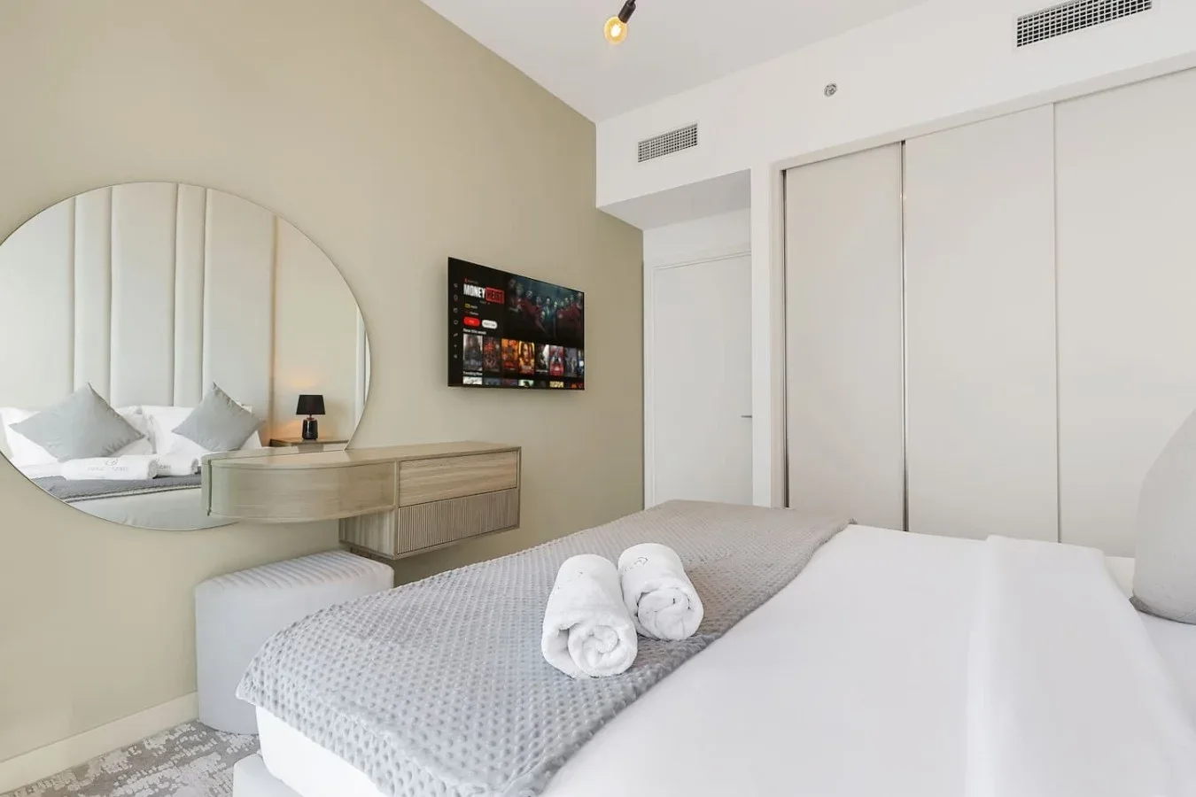 Dormitorio con una cama, un espejo redondo y un televisor montado en la pared.