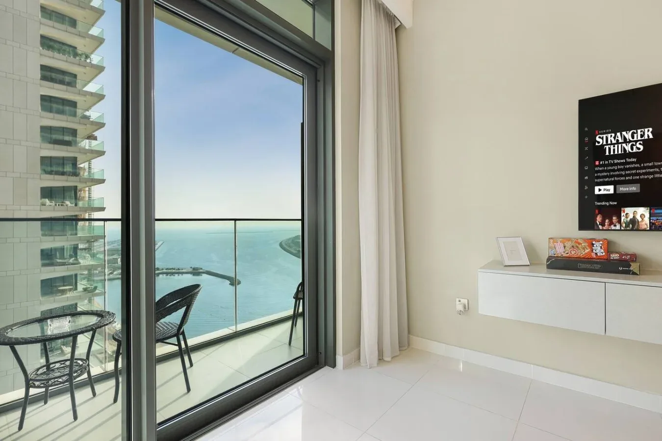 Una habitación luminosa da a un balcón con barandillas de vidrio y vistas al mar.