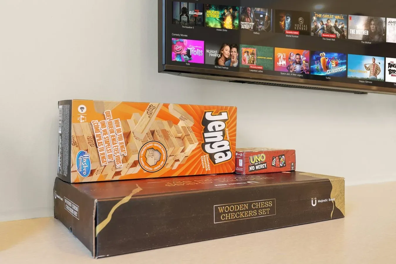 Juegos de mesa, como Jenga y ajedrez de madera, están bajo una pantalla de televisión.