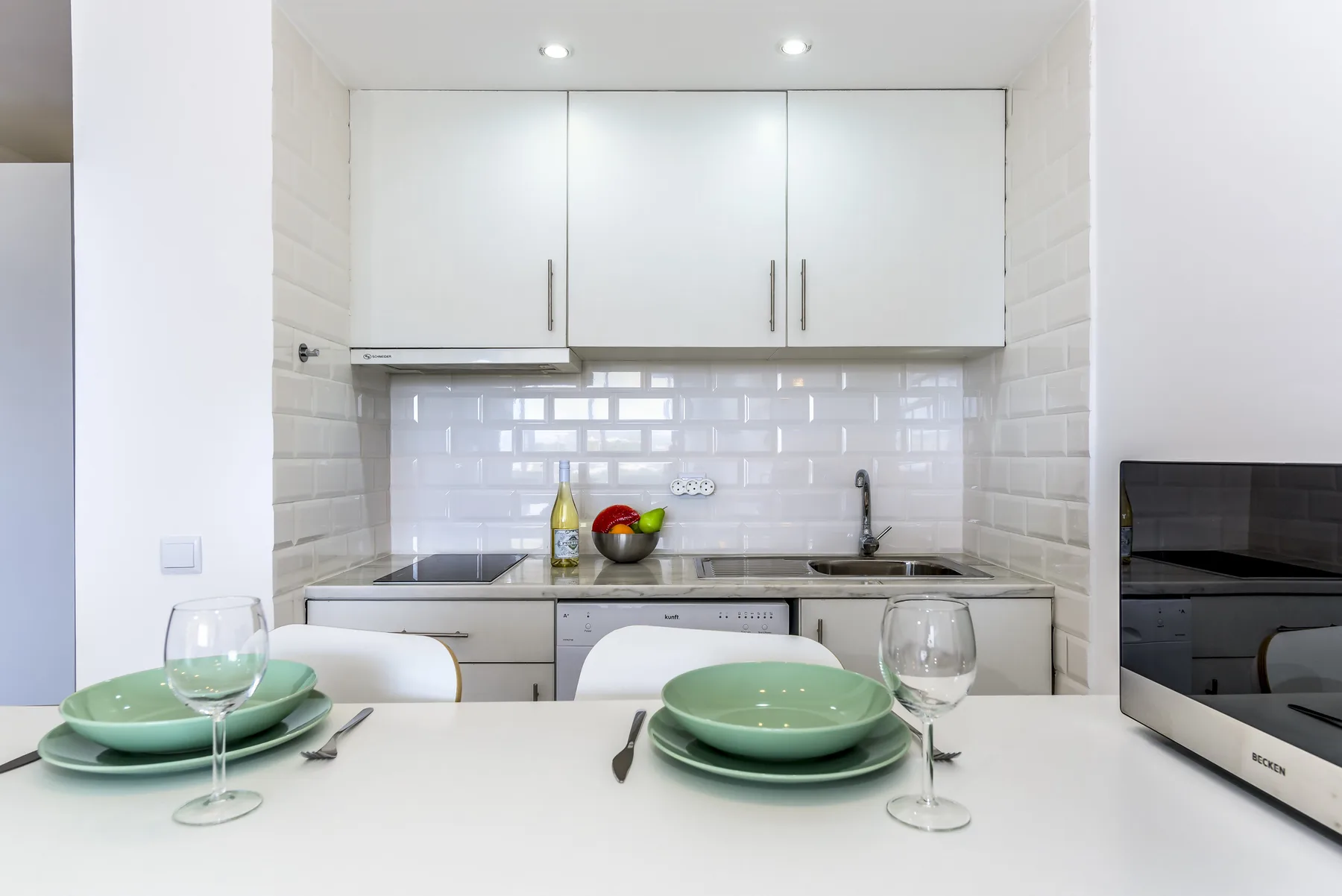 Una cocina luminosa con gabinetes blancos y una mesa puesta con platos verdes.