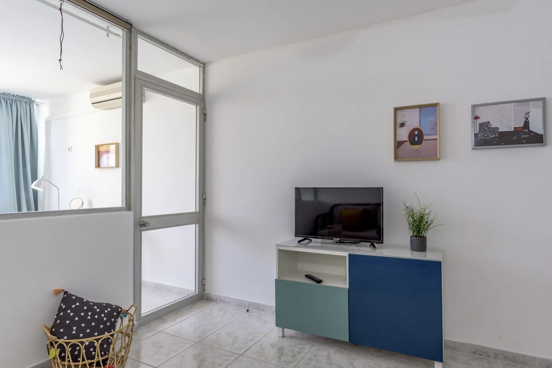 Un salón luminoso tiene un televisor sobre un mueble bajo de colores y cuadros enmarcados.
