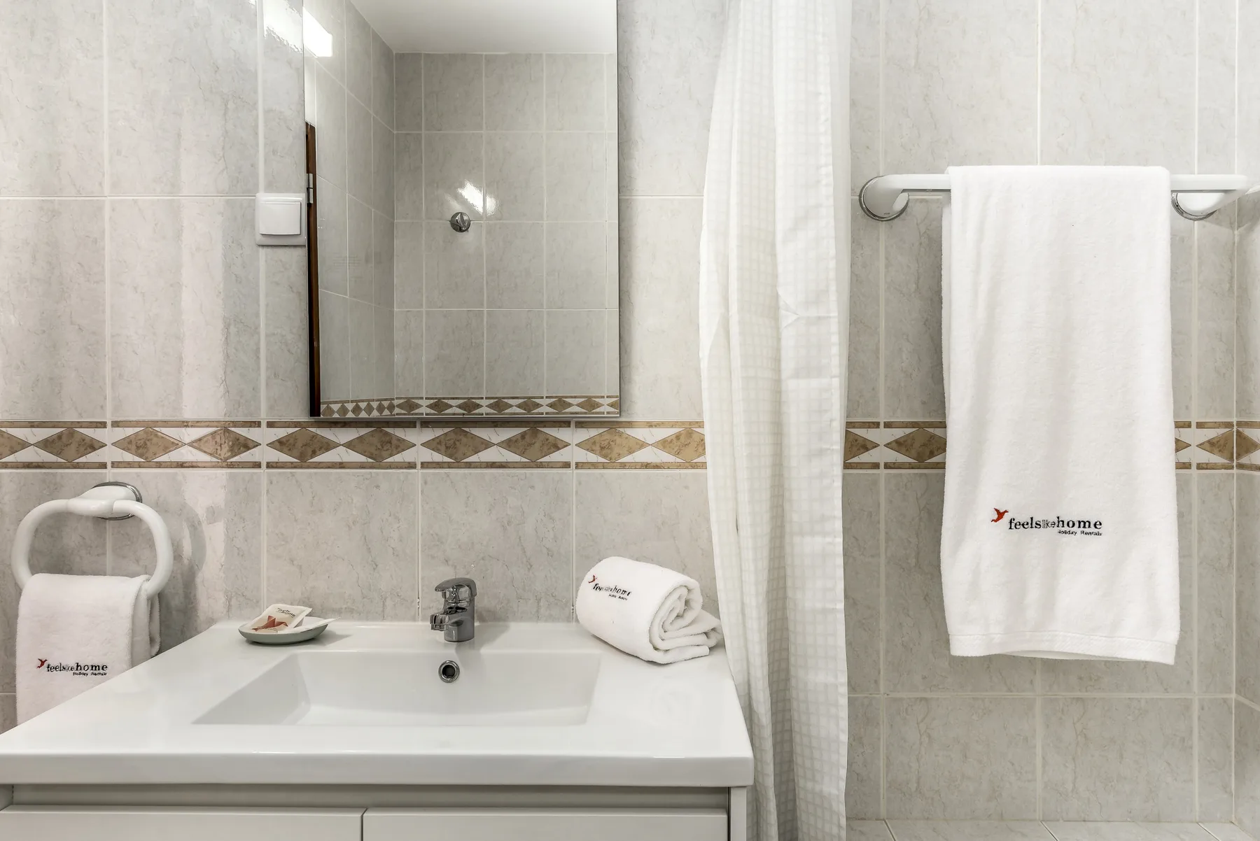 Un baño alicatado con lavabo, espejo y una toalla colgada.