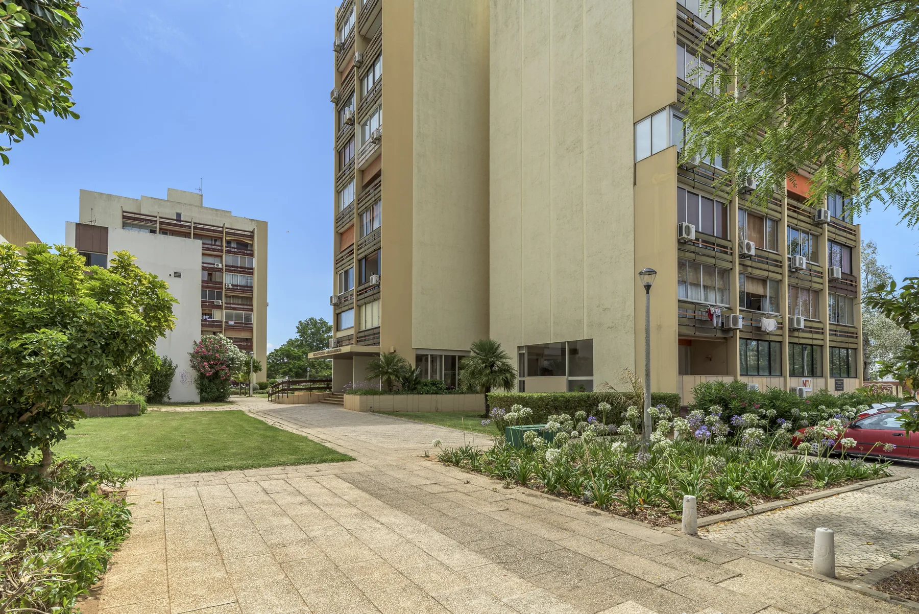 Un camino pavimentado atraviesa jardines junto a un edificio de apartamentos de varias plantas.