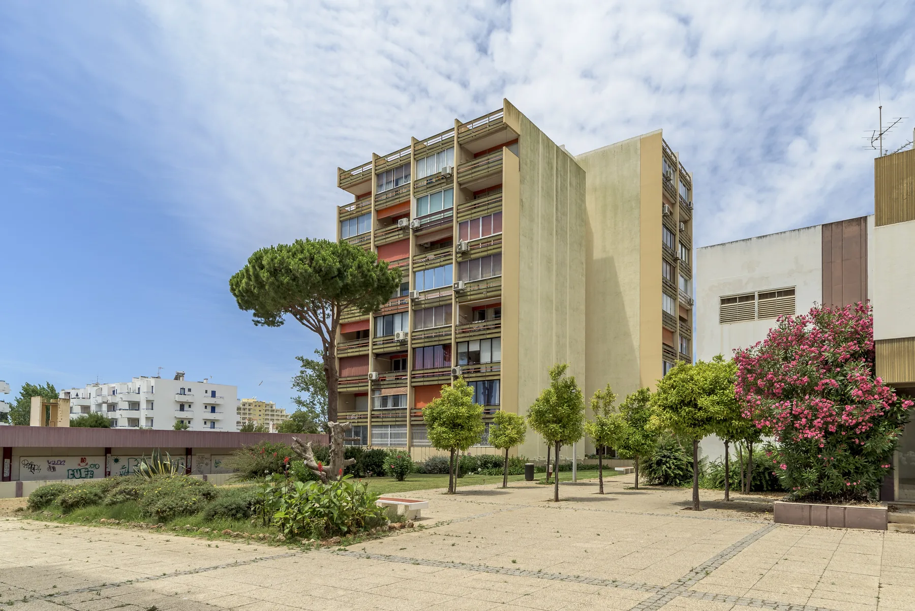 Edificios de apartamentos dan a un patio pavimentado con árboles y arbustos en flor.