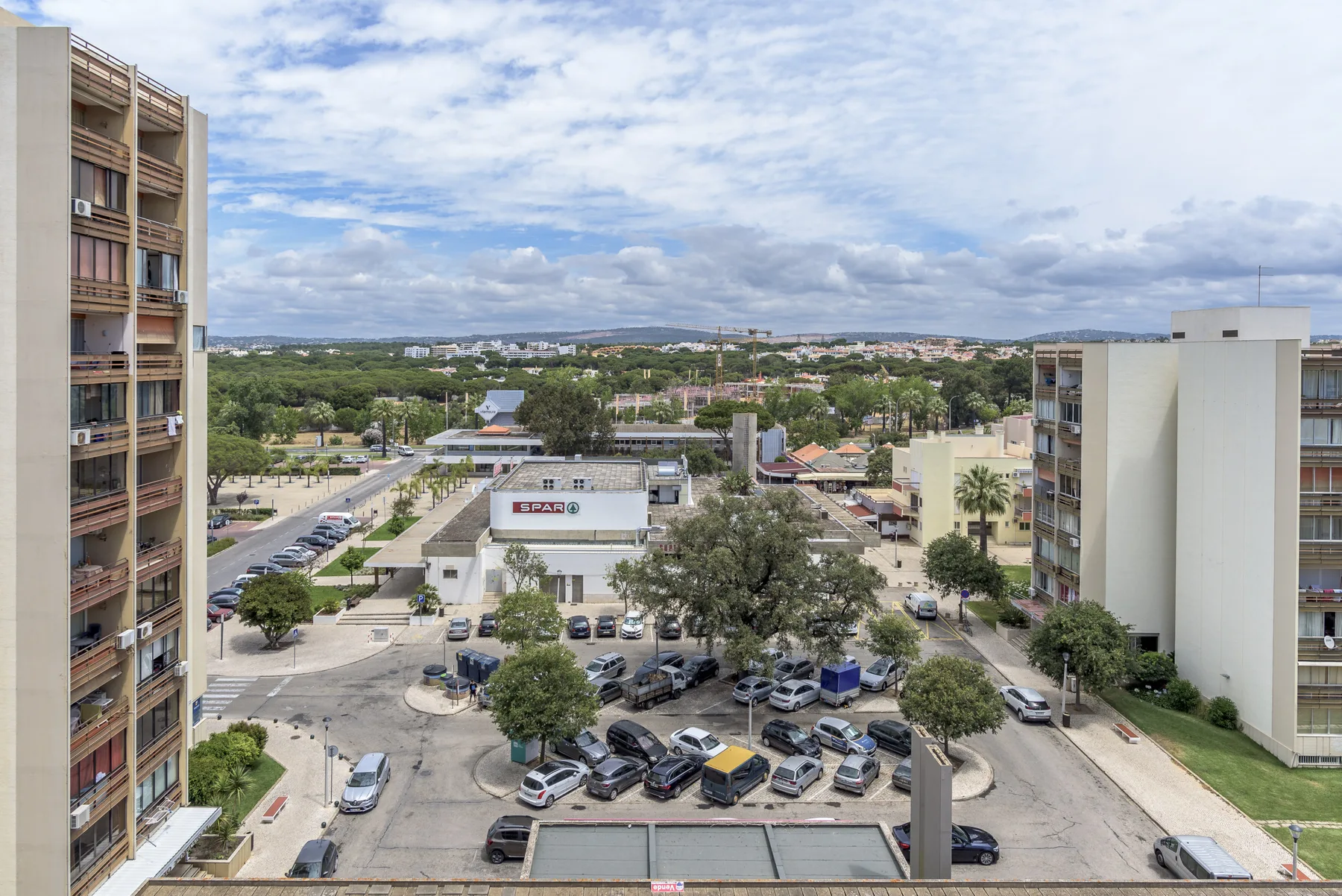 A view over a parking area and low-rise buildings beneath a cloudy sky.