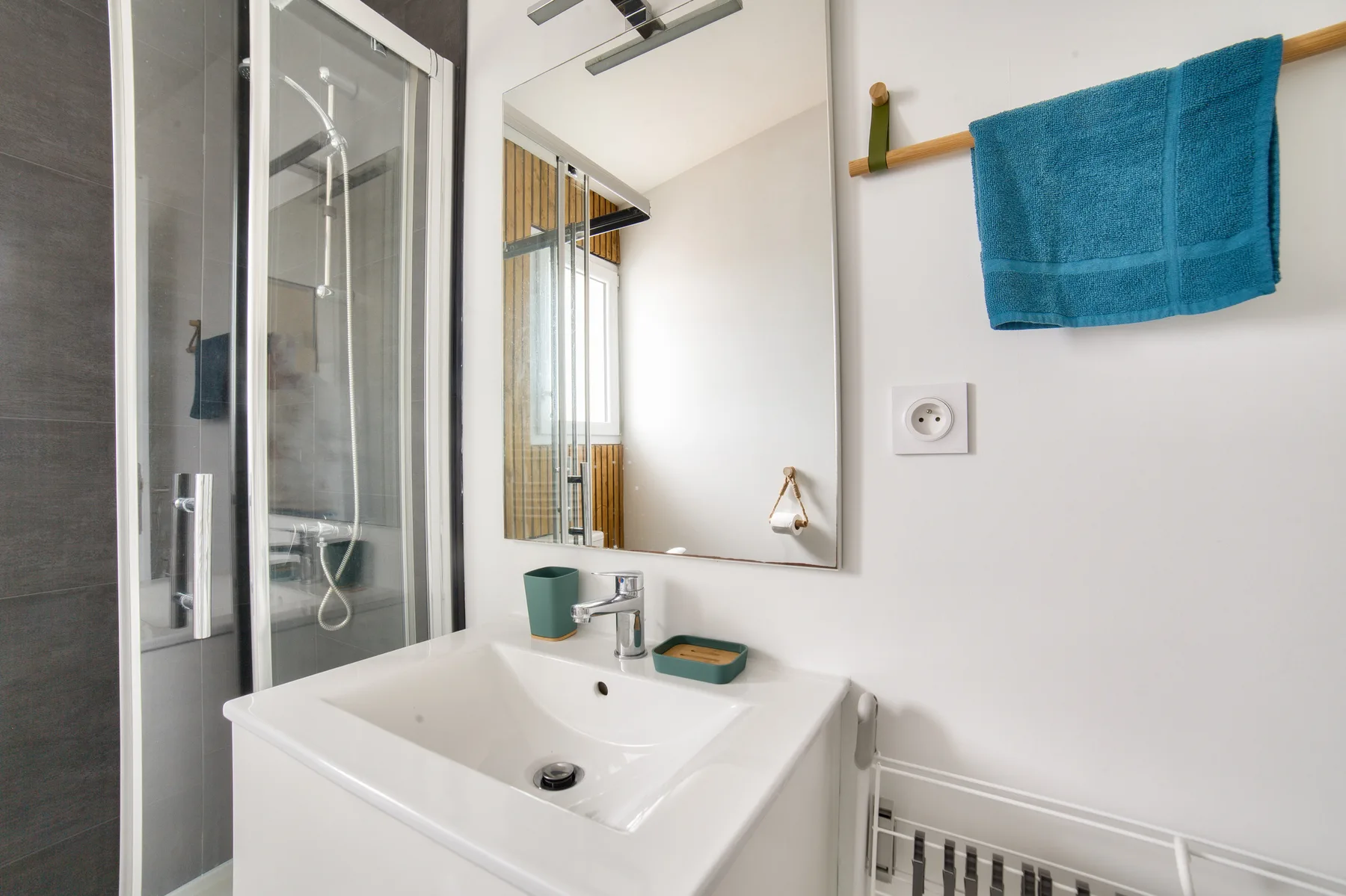 A bathroom sink and mirror are beside a glass-enclosed shower.