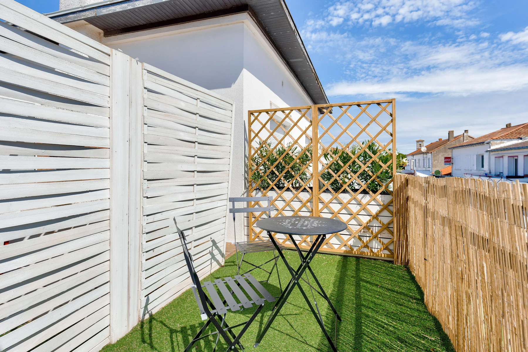 A small outdoor patio with seating, lattice screening, and artificial grass.