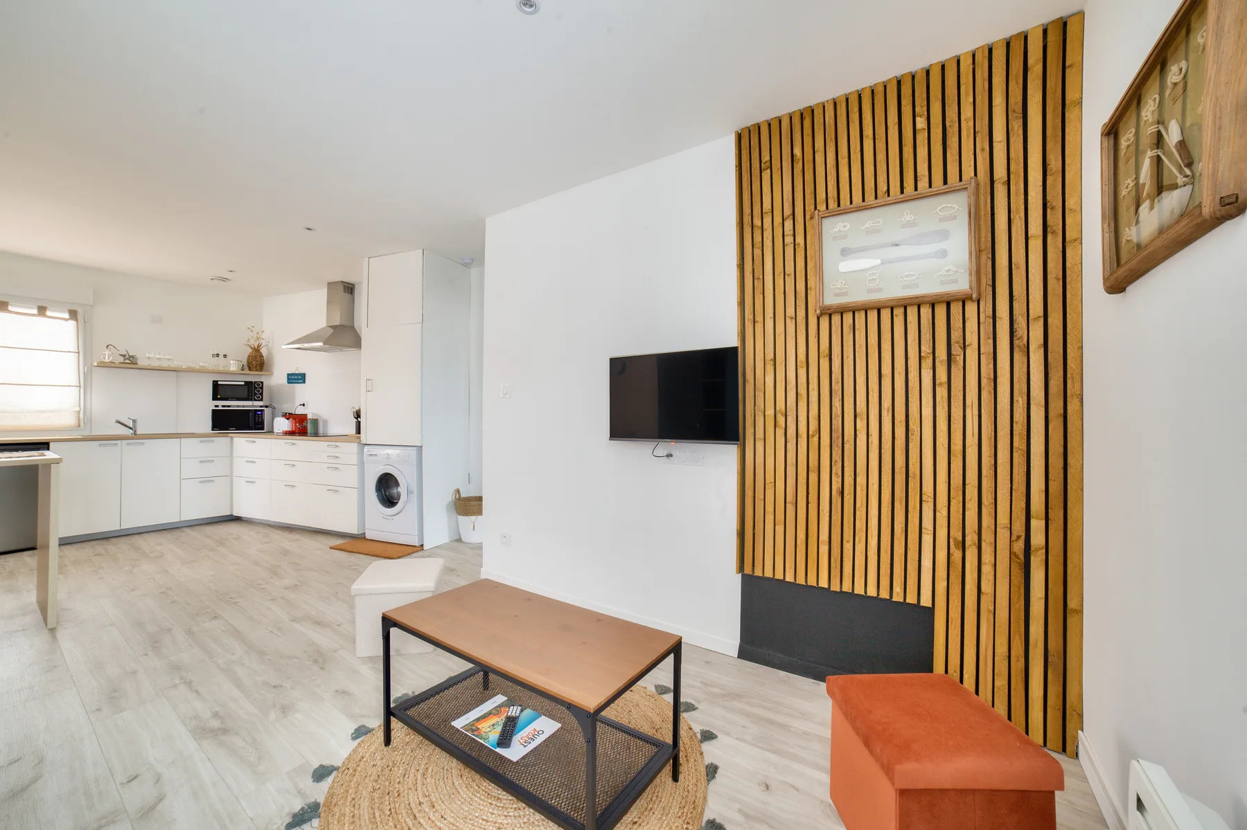 A studio living area with a compact kitchen and a television mounted on the wall.