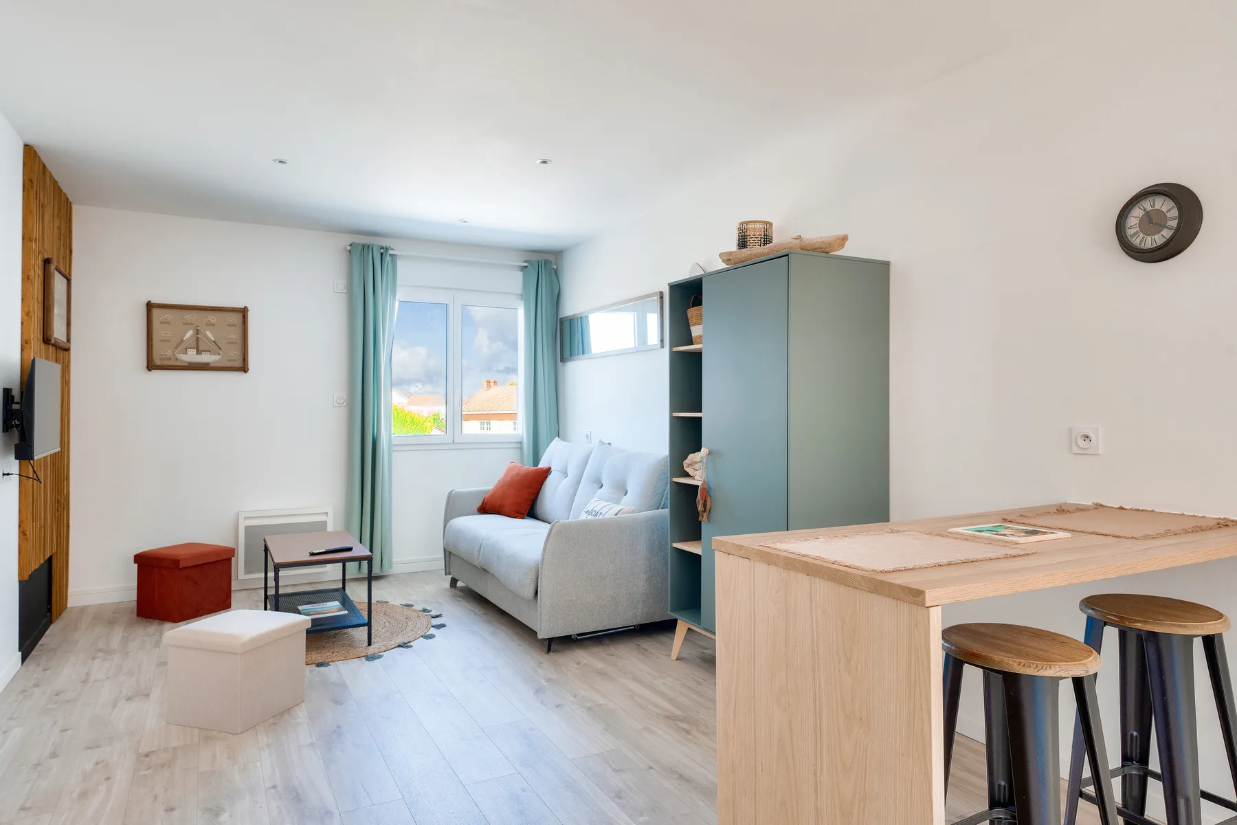 Bright studio living area with a sofa, window, and kitchen counter.