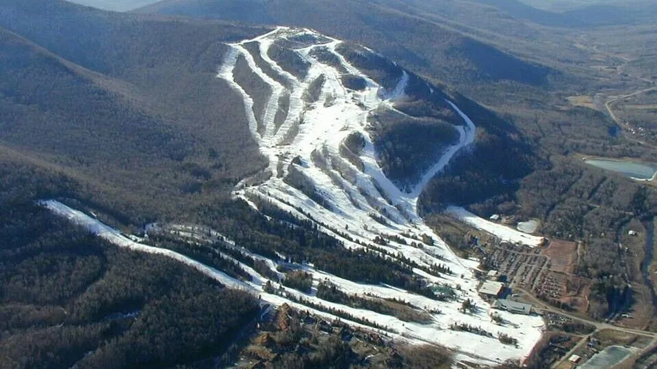 An aerial view of a snow-covered ski slope winding through wooded hills.