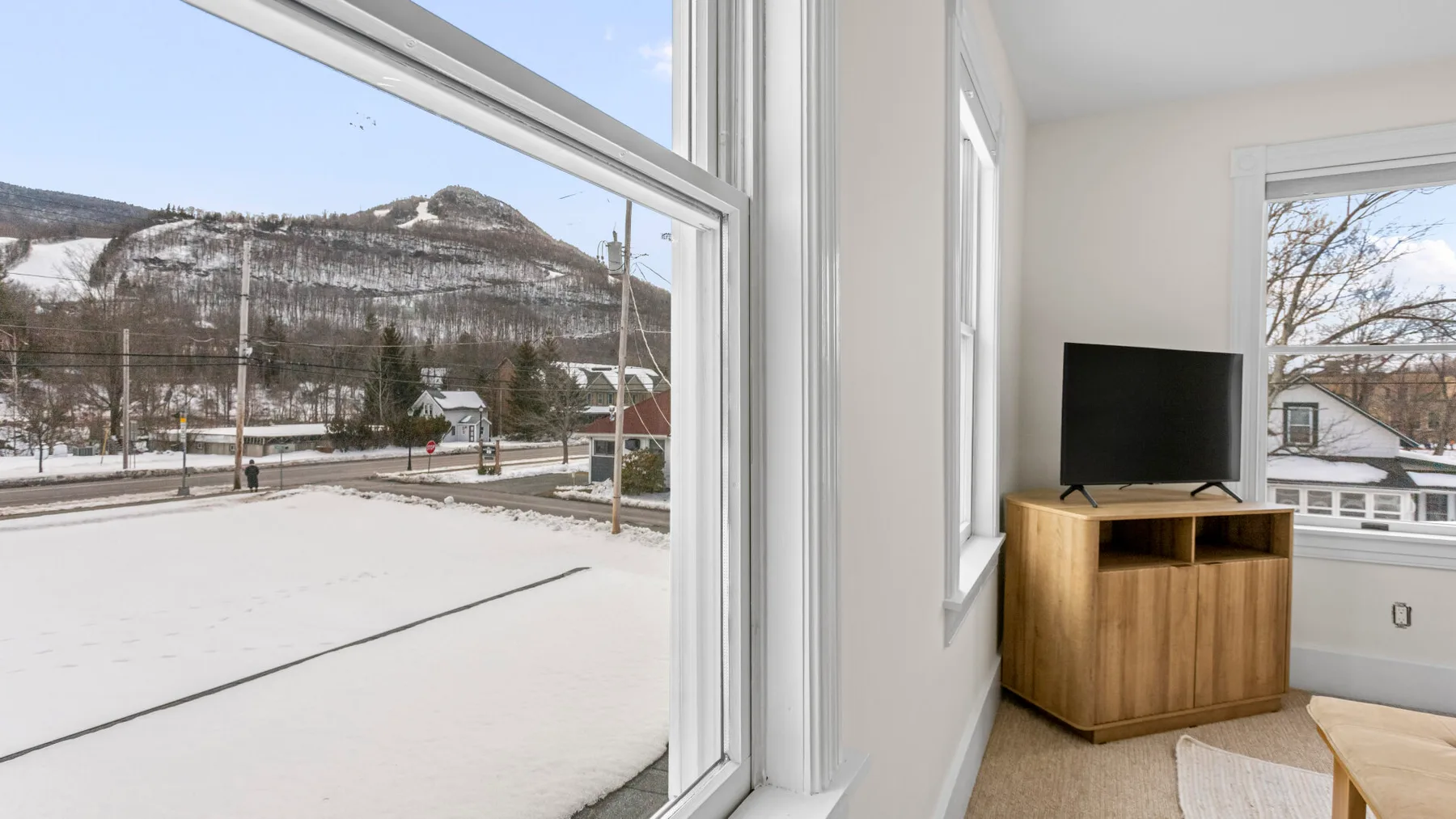 A bright room with a television on a wooden cabinet beside snowy outdoor views.