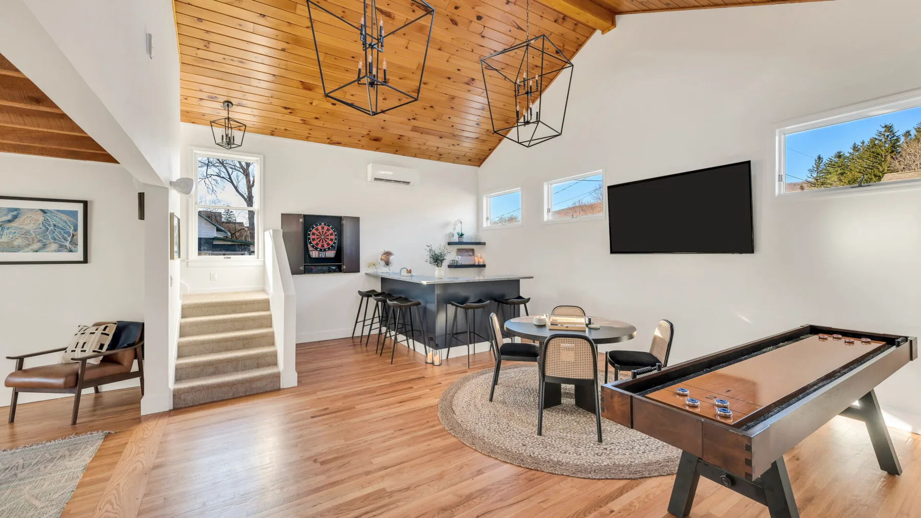 A bright game room with a pool table, dartboard, and high wooden ceiling.