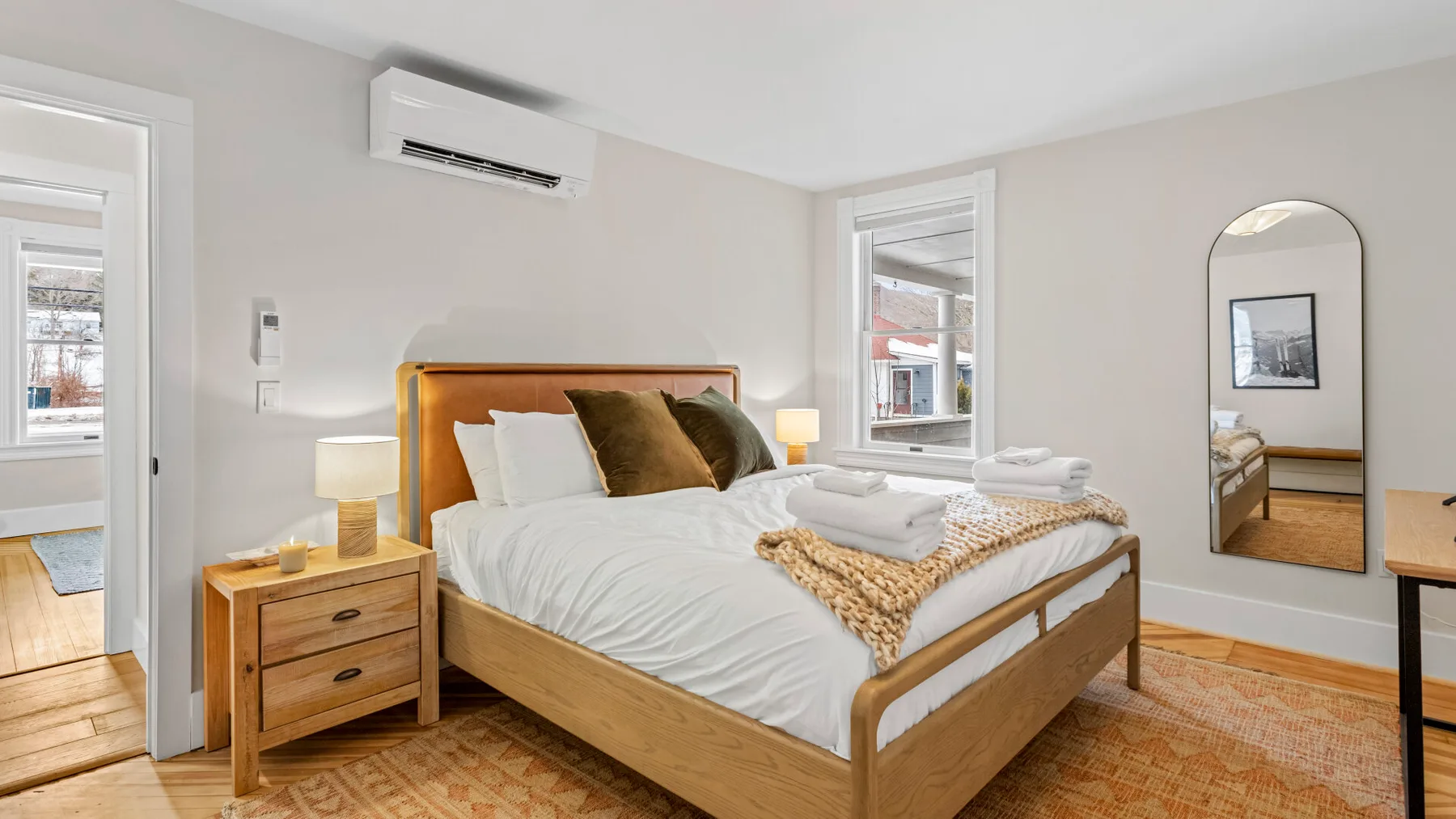 A bright bedroom with a wooden bed, bedside table, and windows.