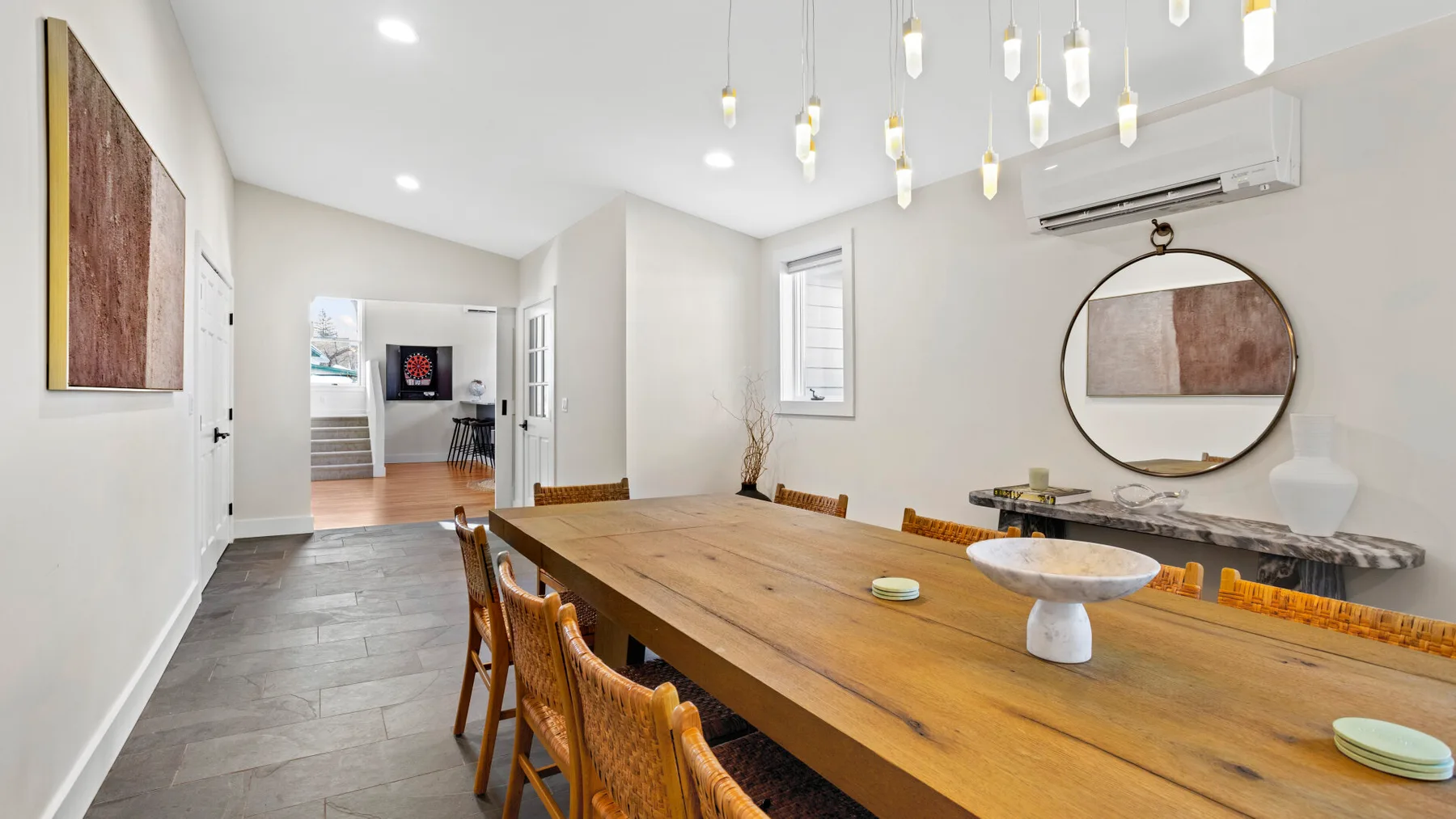 A dining room with a long wooden table beneath hanging lights.