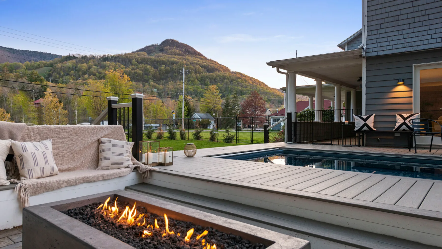 An outdoor deck with a seating area and a long gas fire pit overlooks wooded hills.