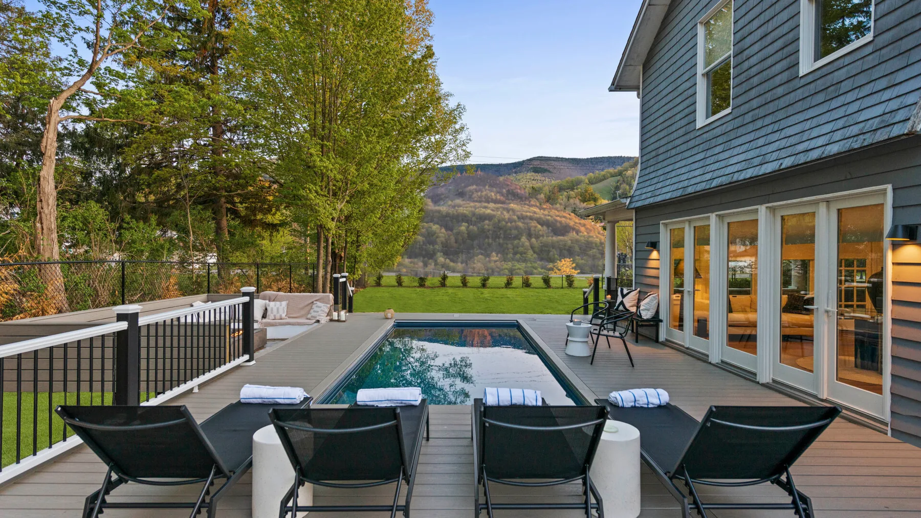 A deck beside the house overlooks a swimming pool and wooded hills.