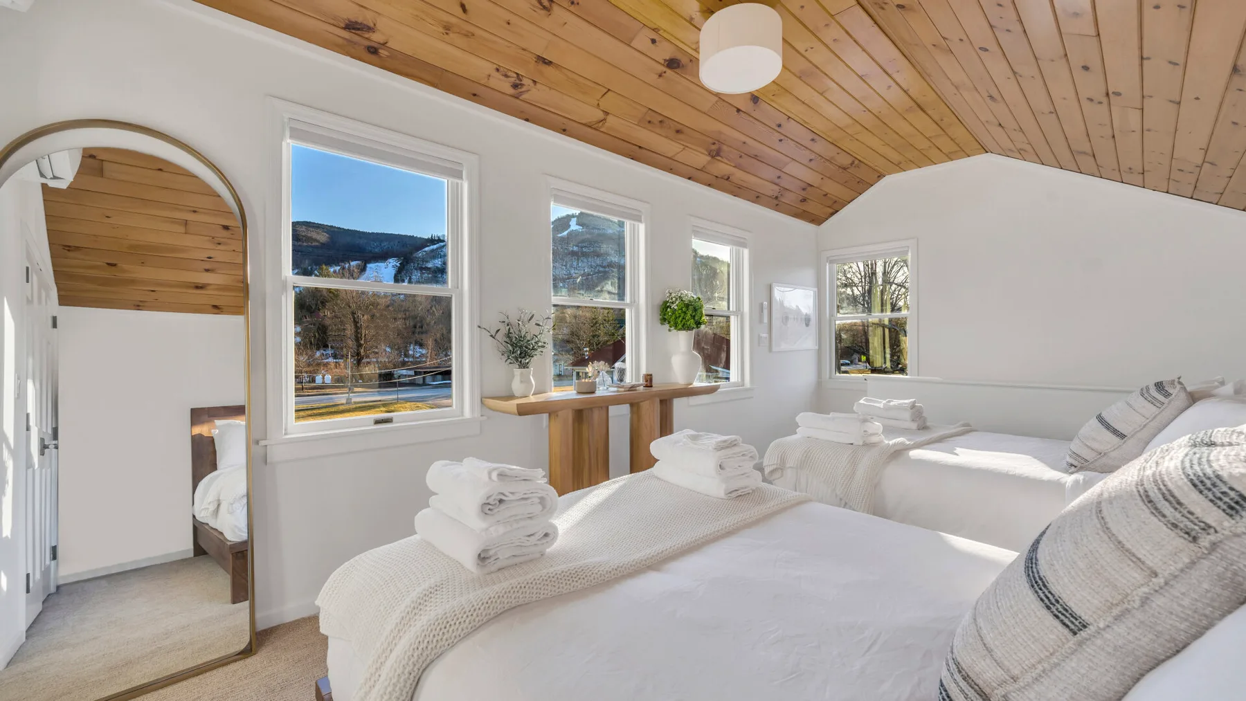 A bright bedroom with several beds, white bedding, and large windows.
