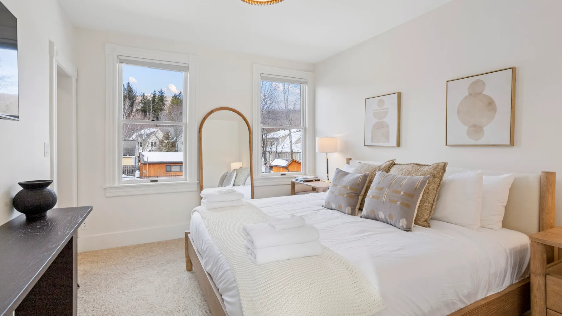 A bright bedroom with a neatly made bed and two tall windows.