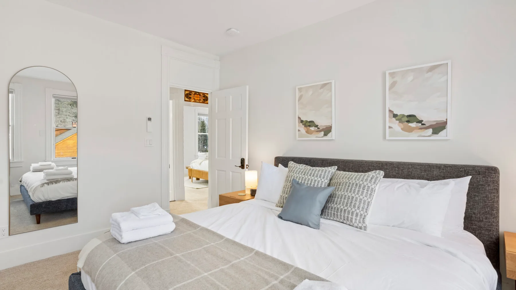 A bright bedroom with a neatly made bed and framed artwork above the headboard.