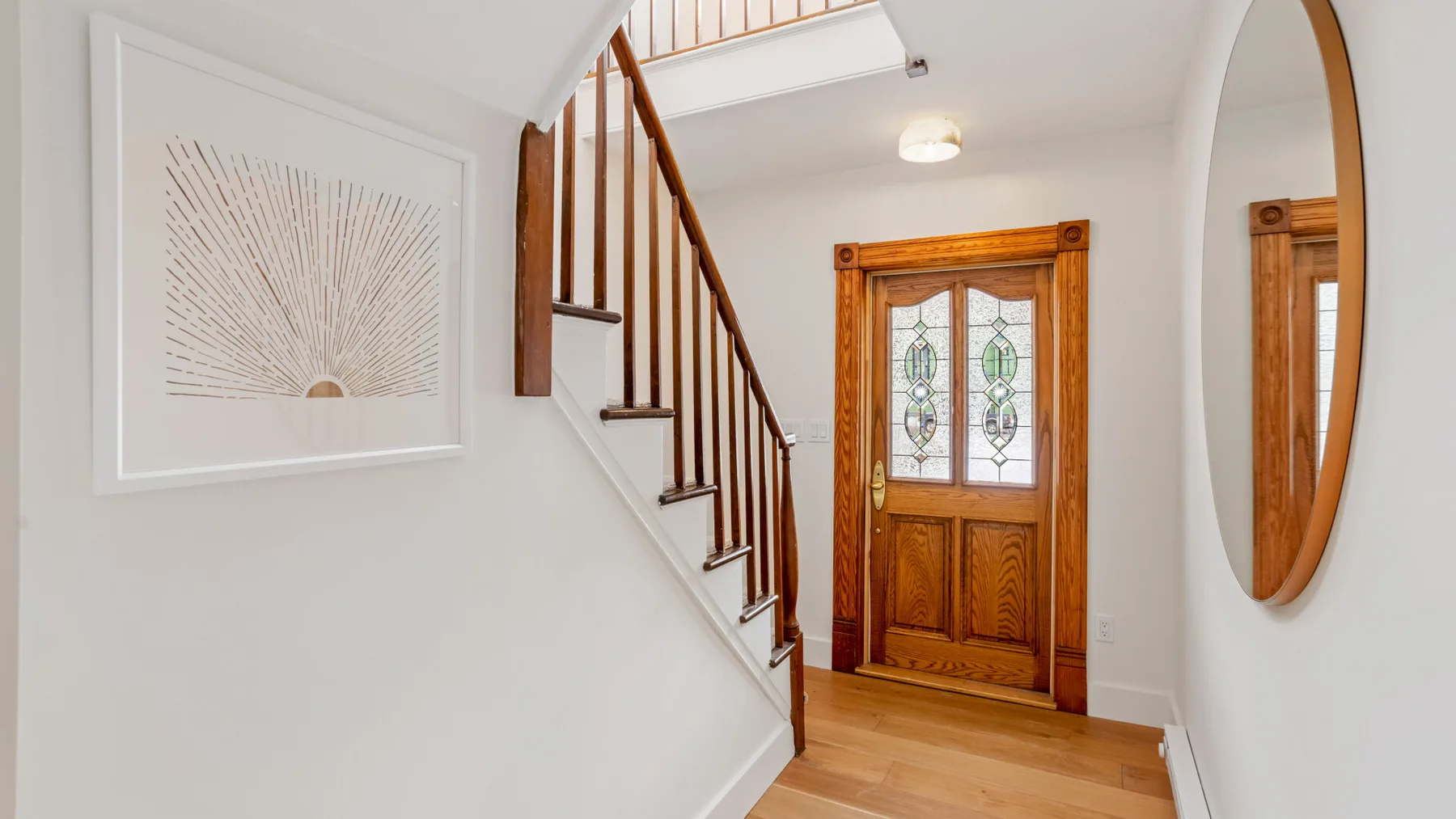 A bright entry hall with a wooden staircase and decorative front door.