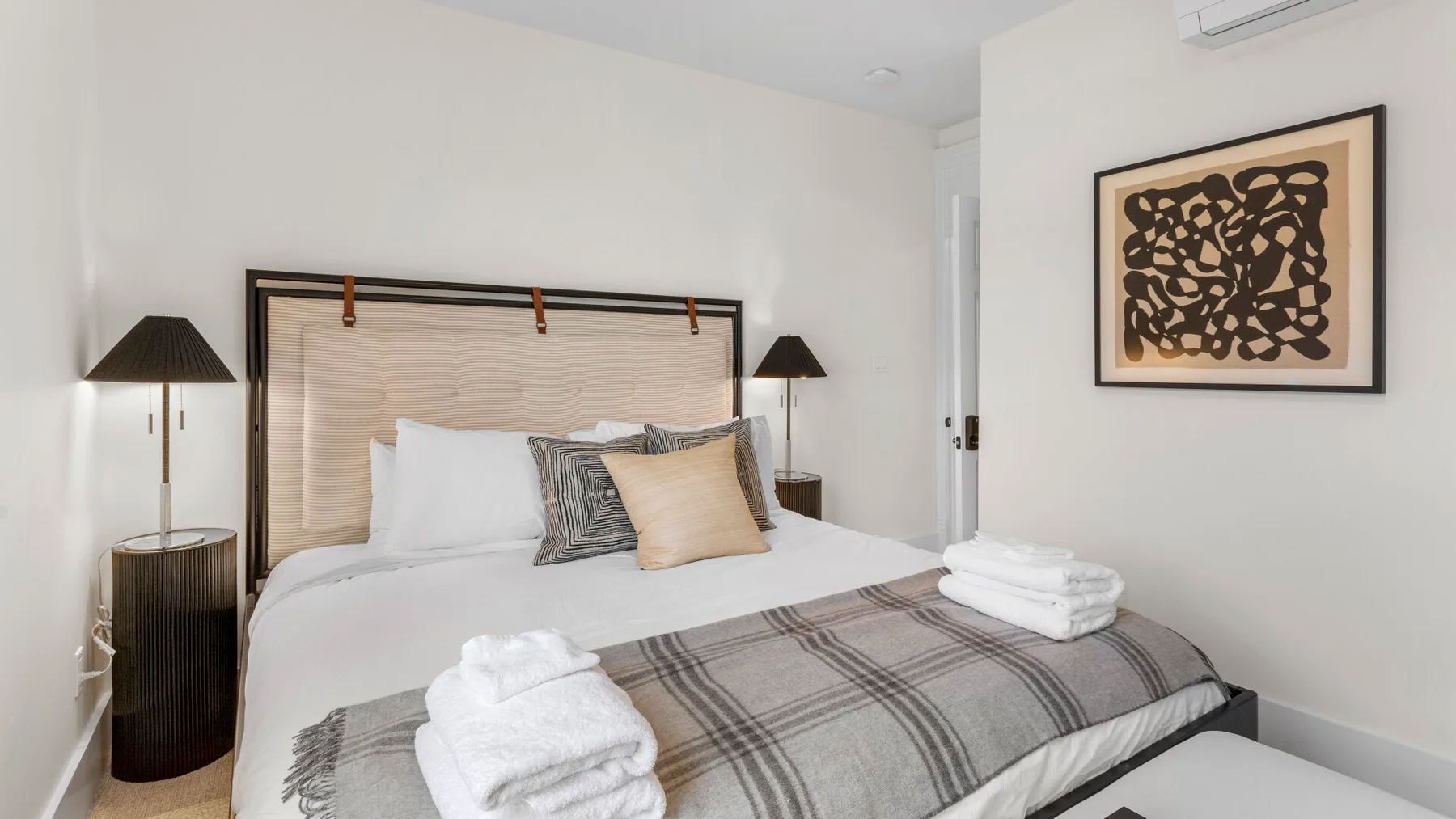 A bedroom with a neatly made bed, folded towels, and framed artwork.