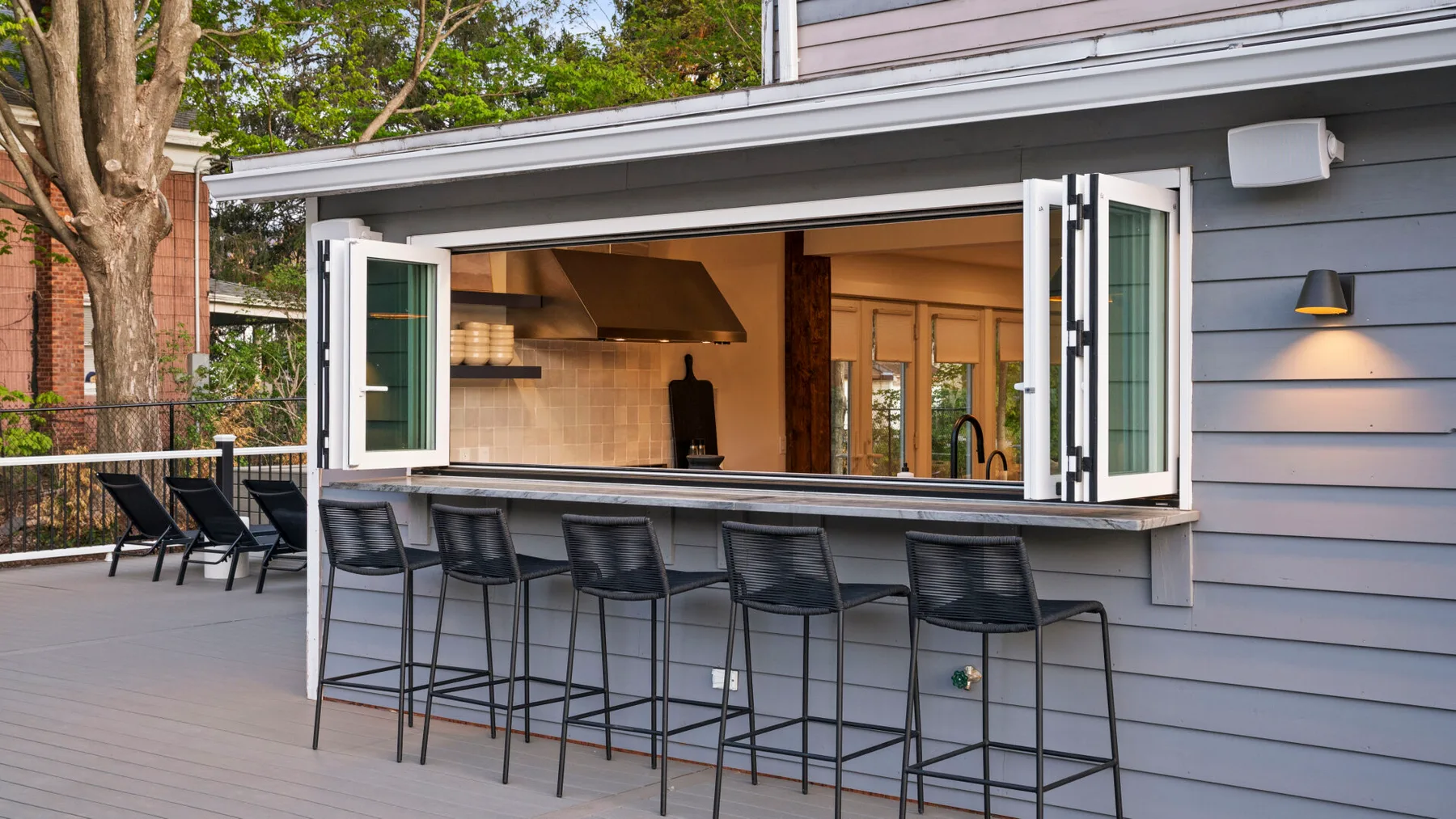 An outdoor counter with bar seating opens onto a kitchen.