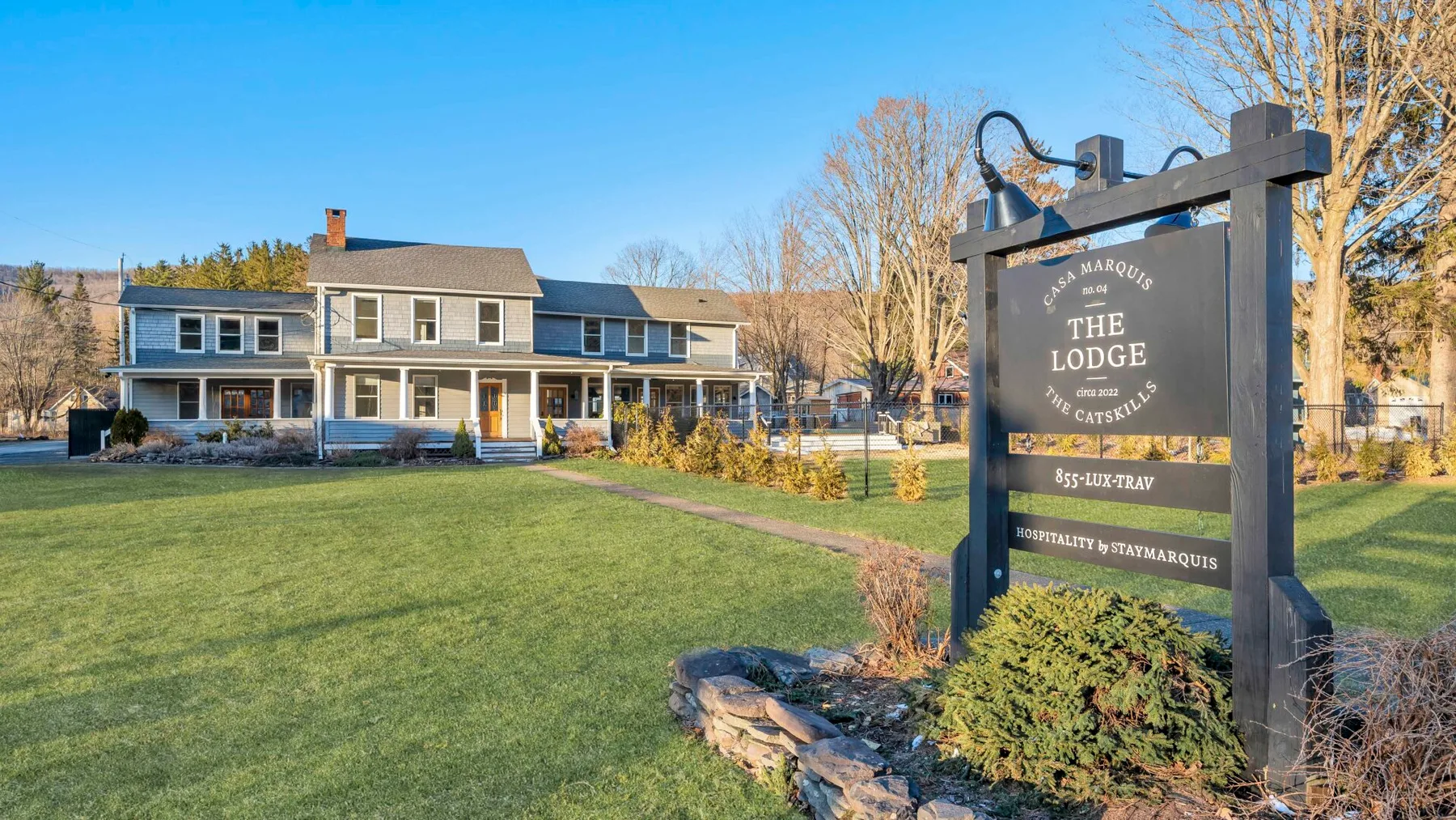 A large lodge building stands behind a lawn, beside a prominent roadside sign.