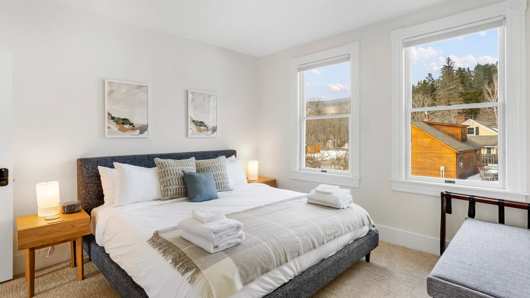A bright bedroom with a neatly made bed and large windows.