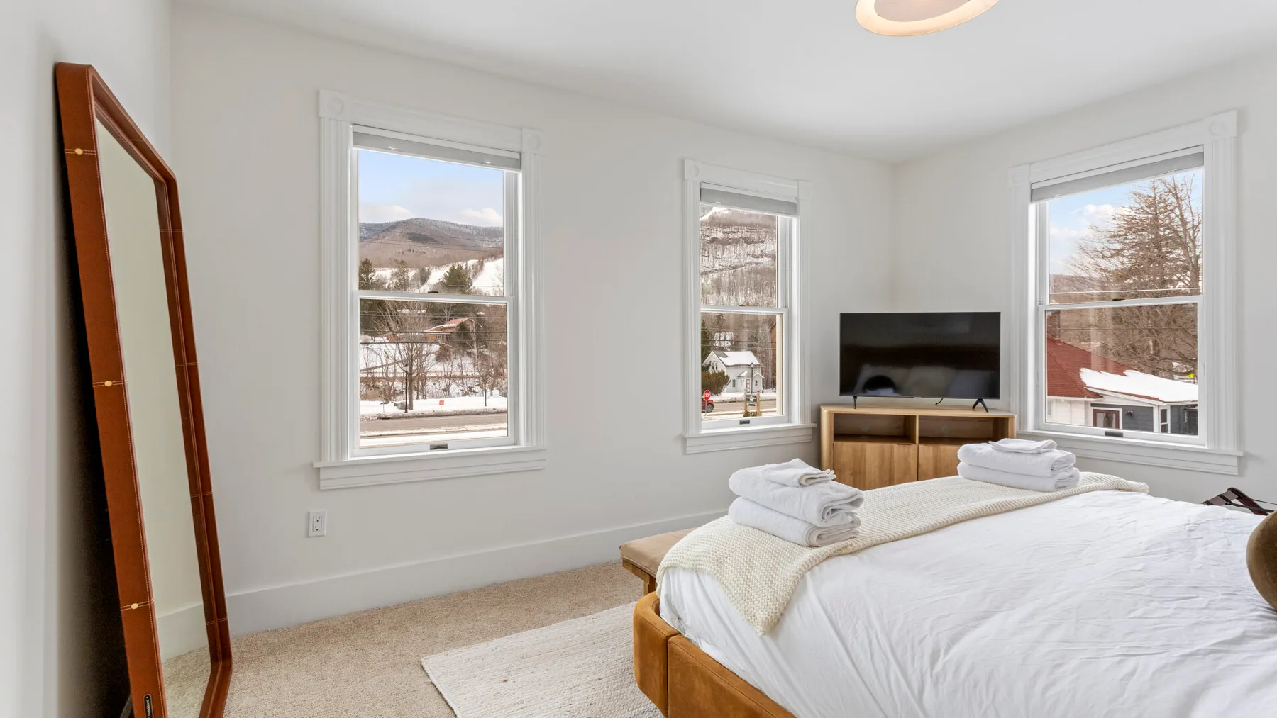 A bright bedroom with a bed and three windows overlooking a snowy landscape.