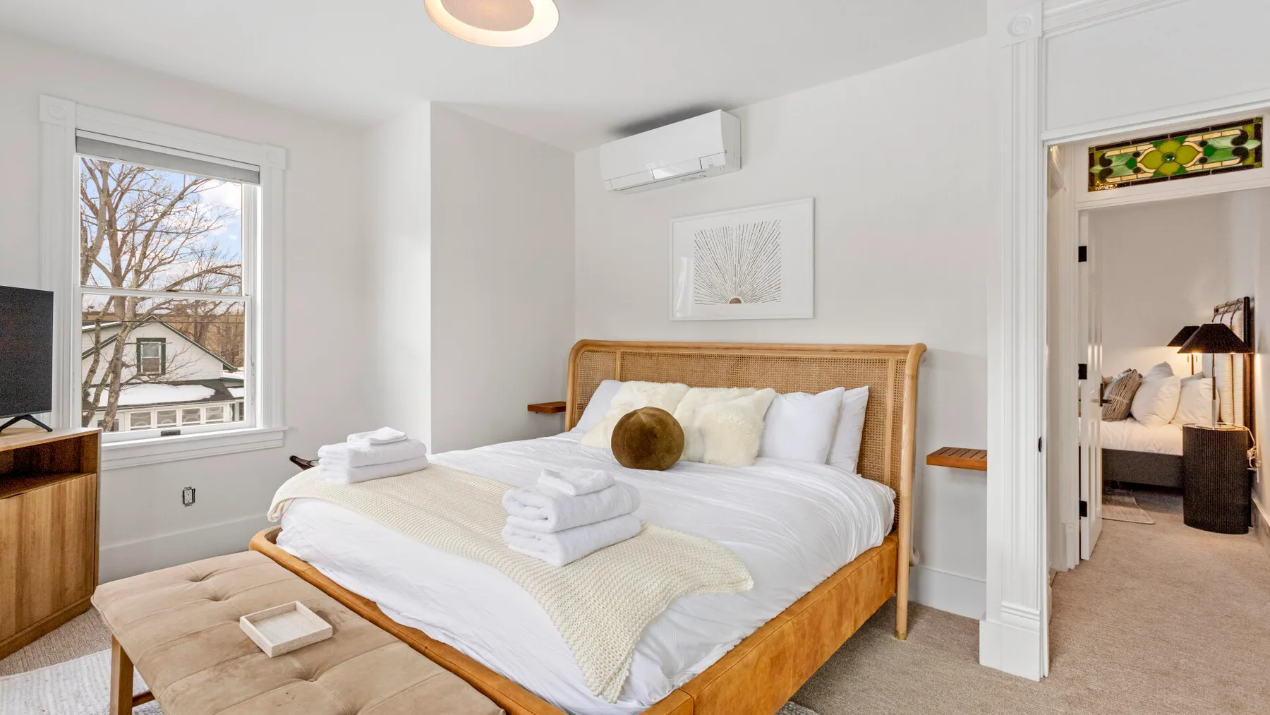 A bright bedroom with a wooden bed, white bedding, and a large window.