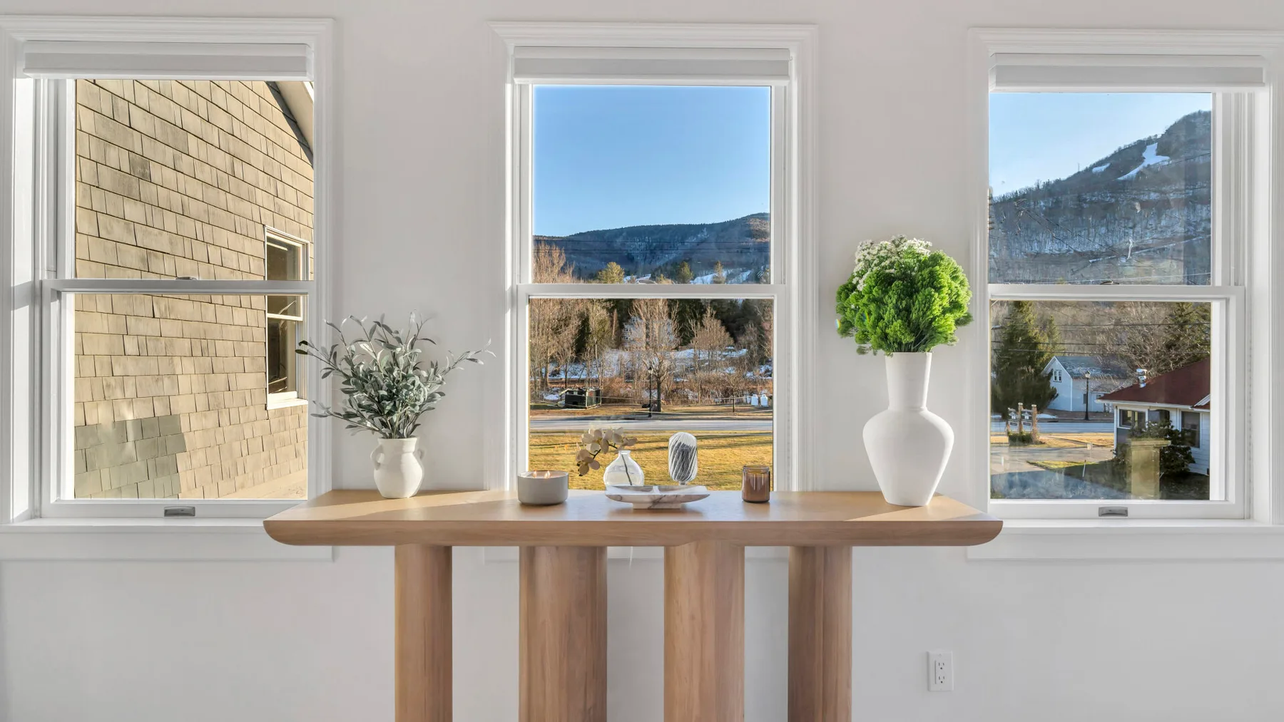 A bright room with a wooden table set beneath three windows.