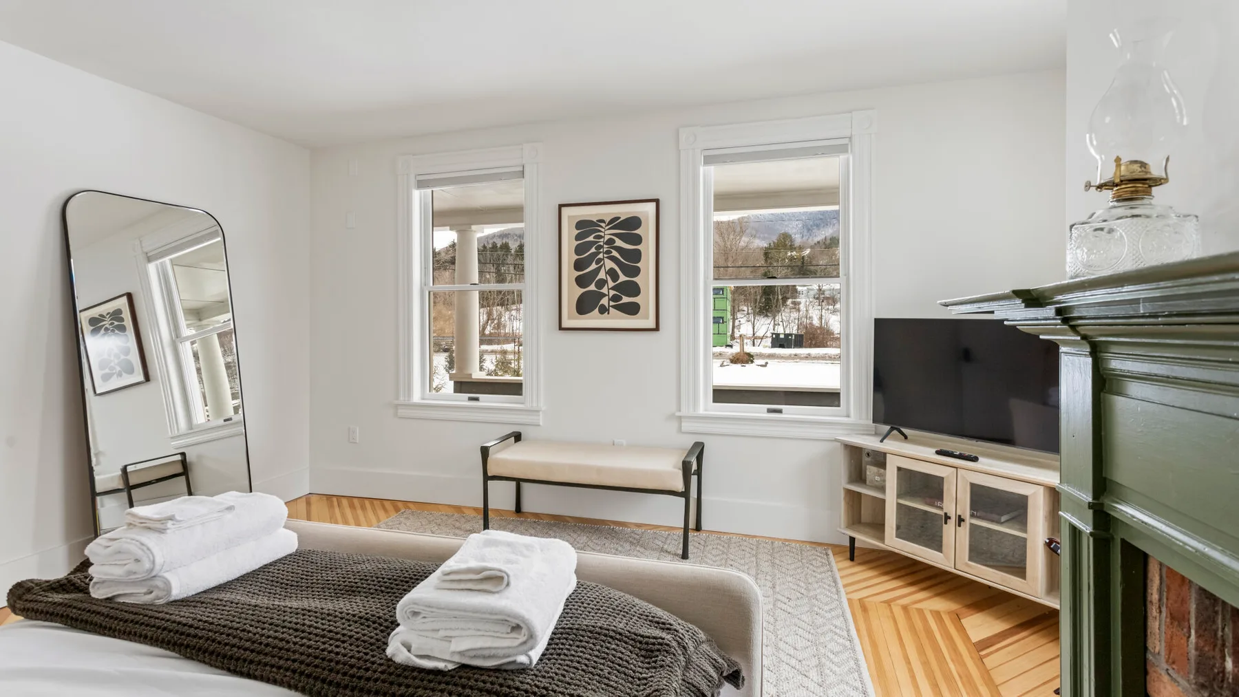 A bright bedroom with a neatly made bed beneath two windows.