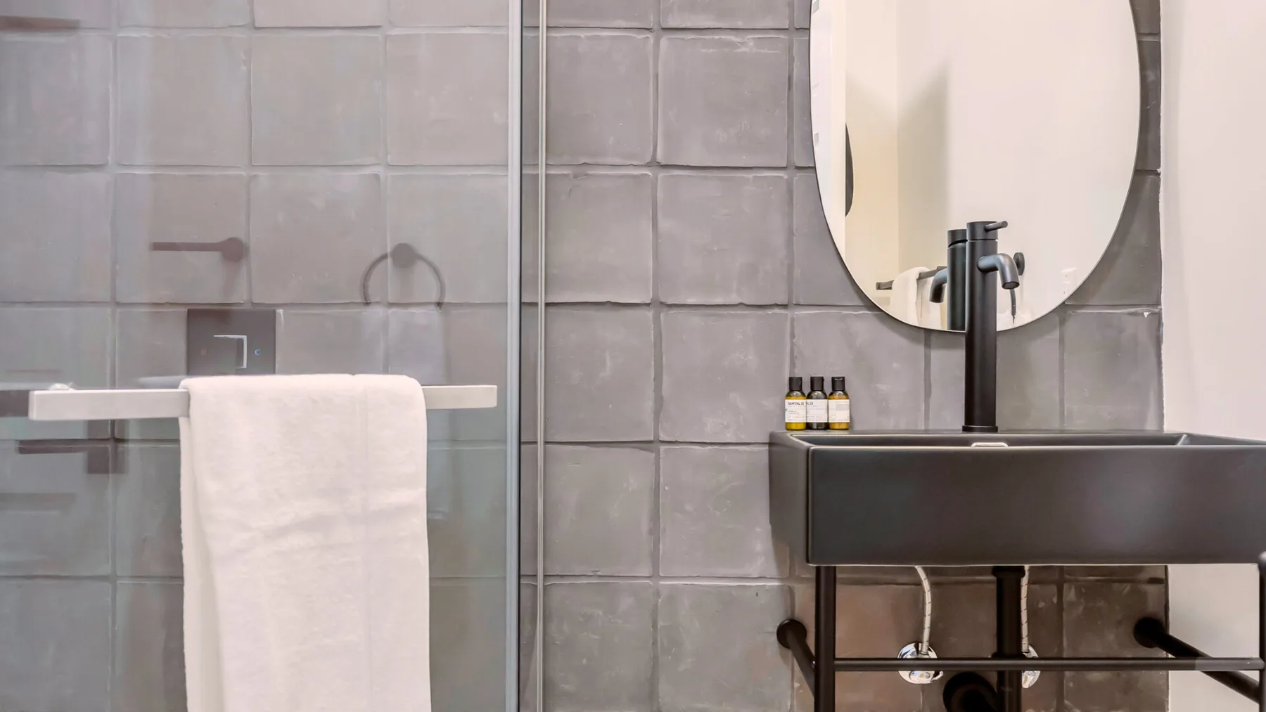 A tiled bathroom with a dark sink, oval mirror, and towel.