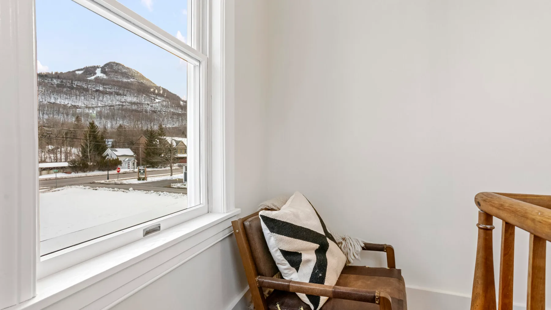 A wooden armchair sits beside a large window overlooking a snowy landscape.