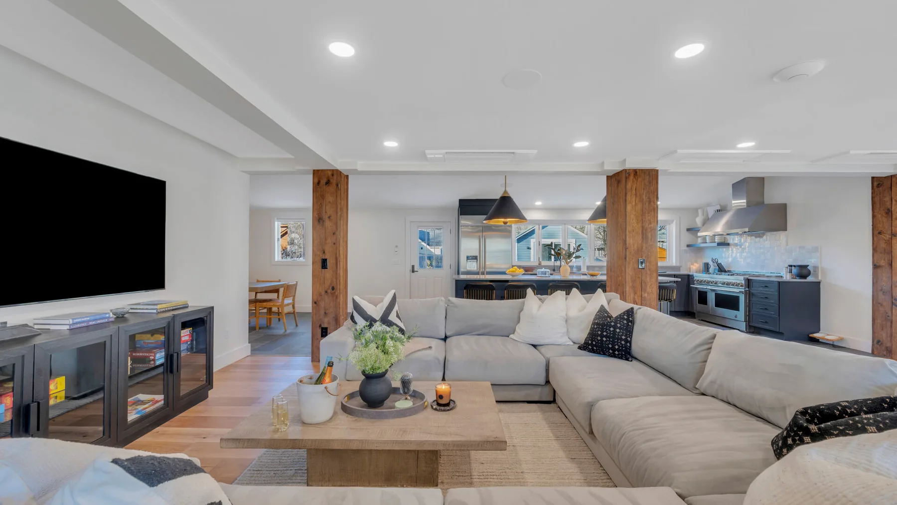 A bright open-plan living room with sectional seating and a kitchen in the background.