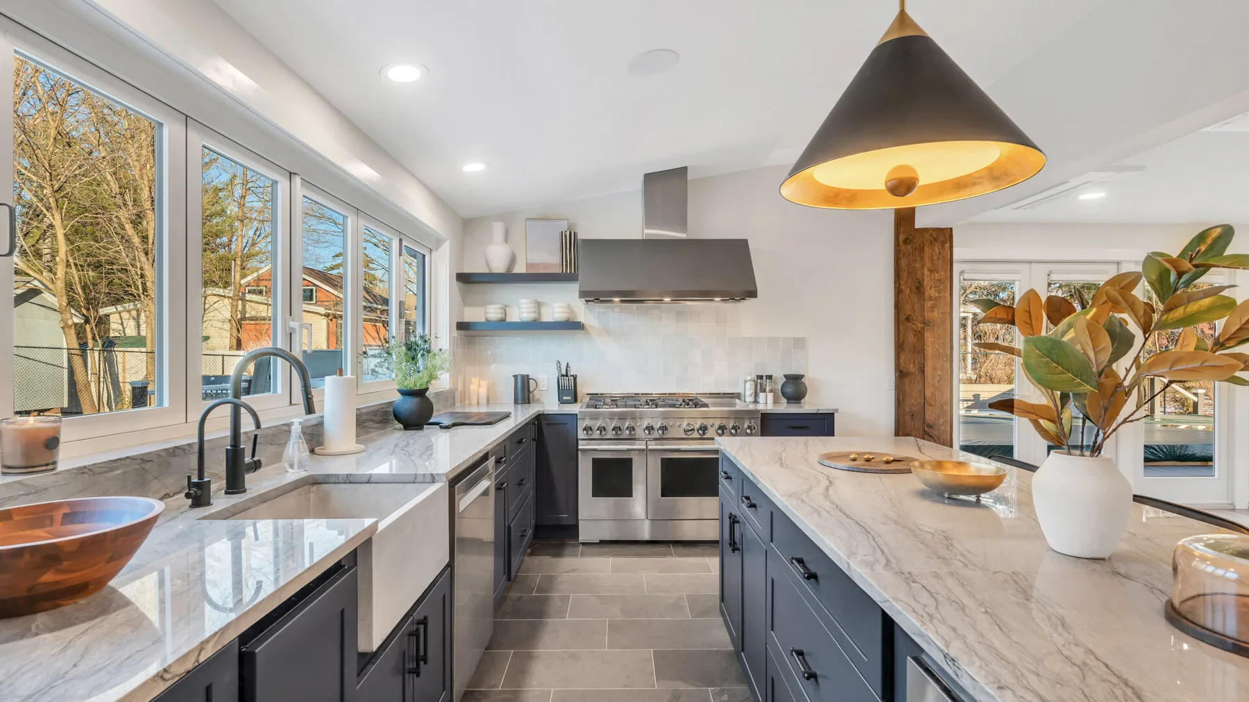 A bright modern kitchen with a central island, dark cabinetry, and large windows.