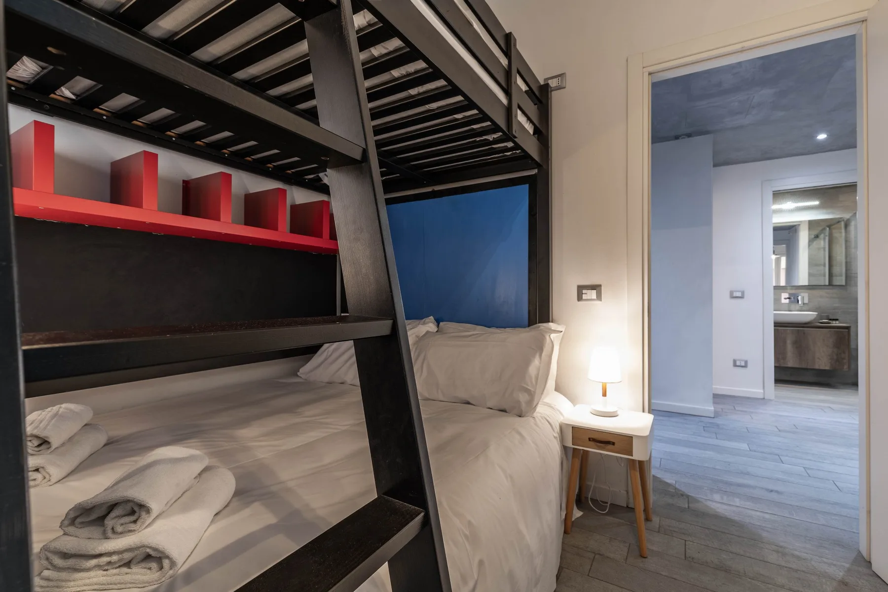 Un dormitorio con una litera negra y una puerta abierta hacia un baño.