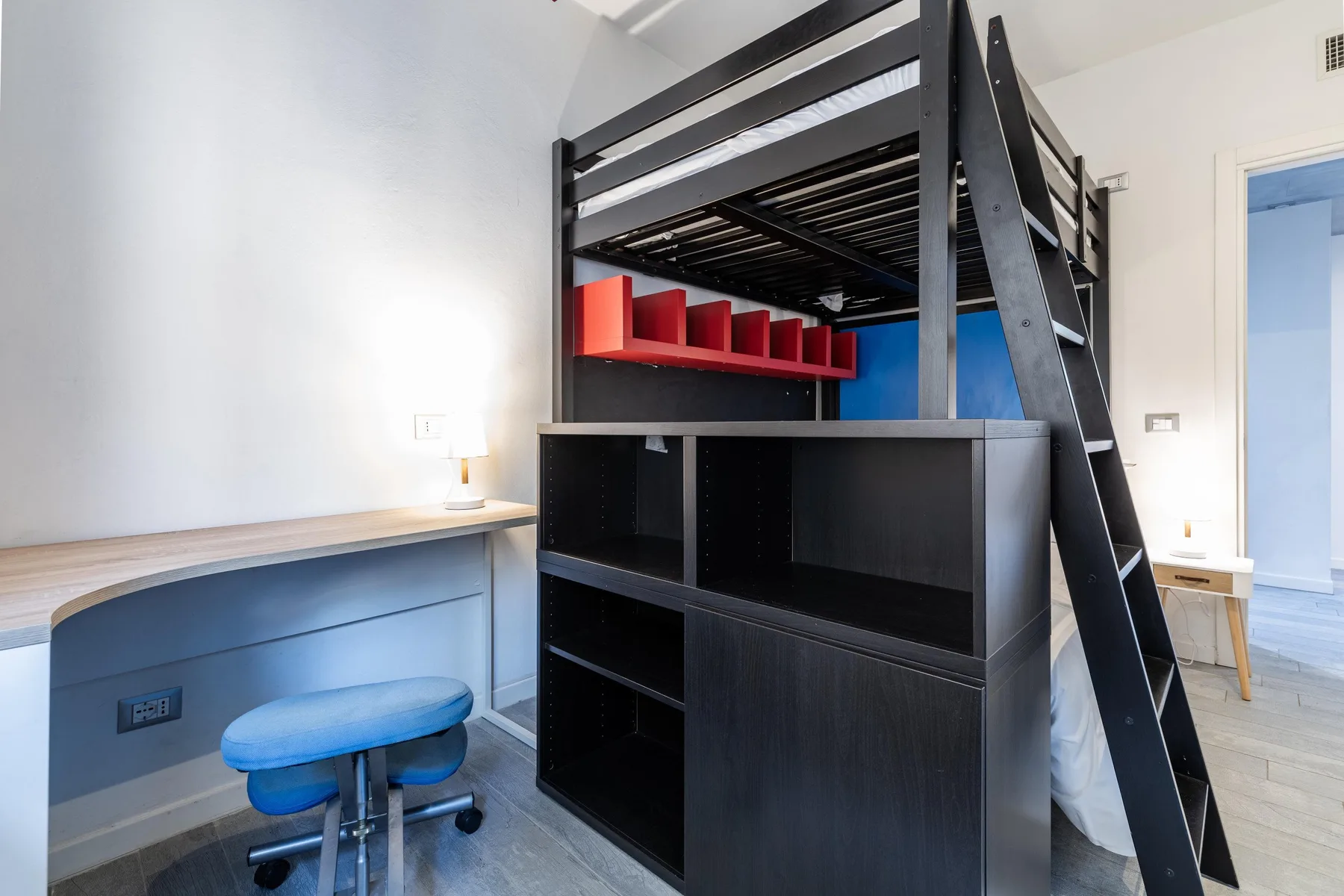 Un dormitorio con una cama alta negra sobre estanterías empotradas y un escritorio.