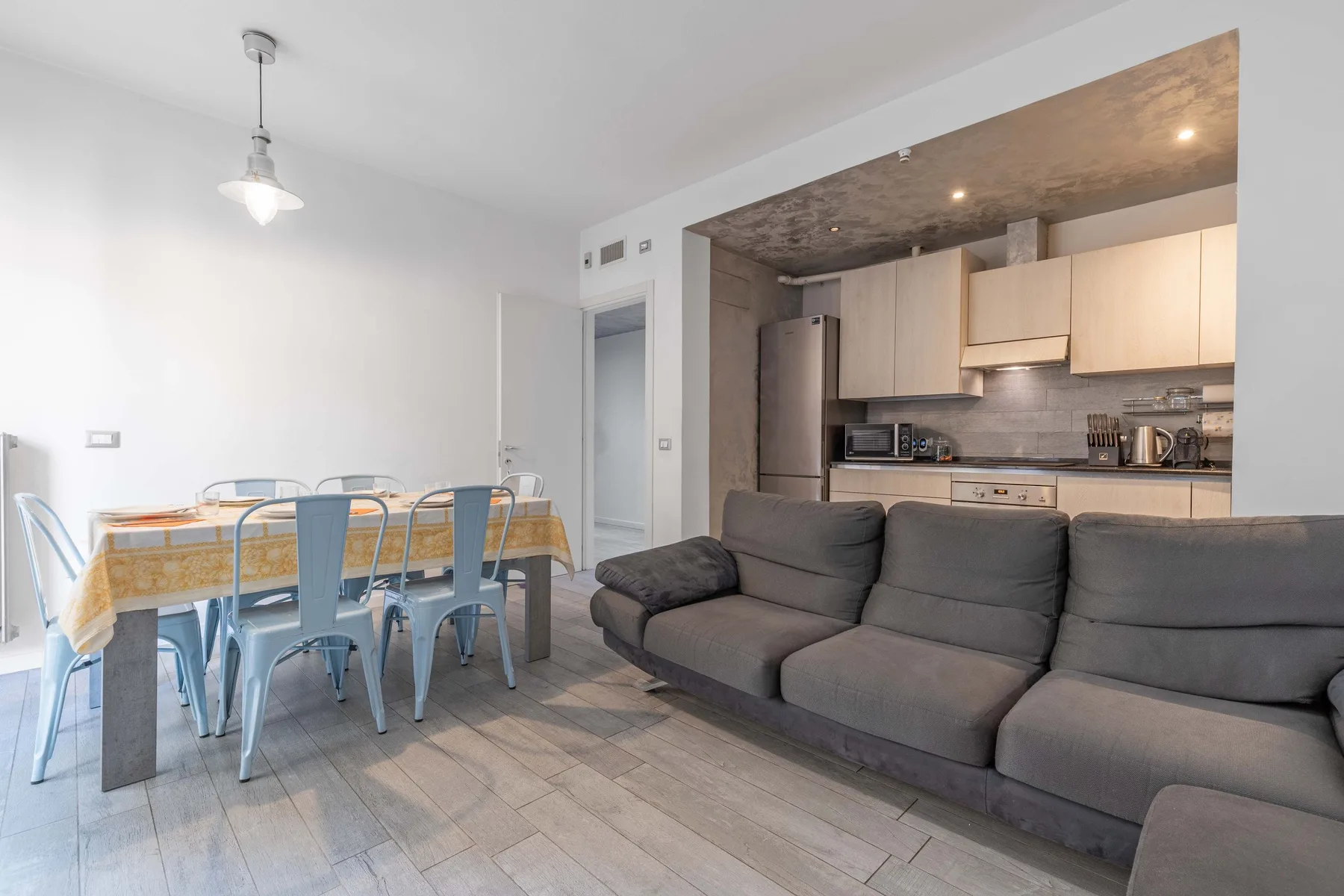 Una sala-comedor abierta con un sofá gris y una cocina.