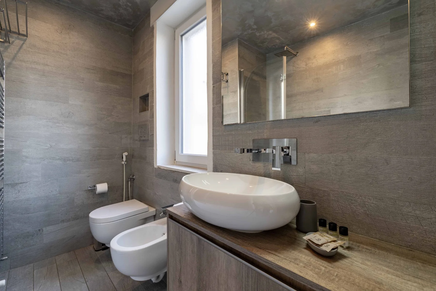 Un baño moderno con lavabo sobre encimera, grifo de pared, inodoro y bidé.