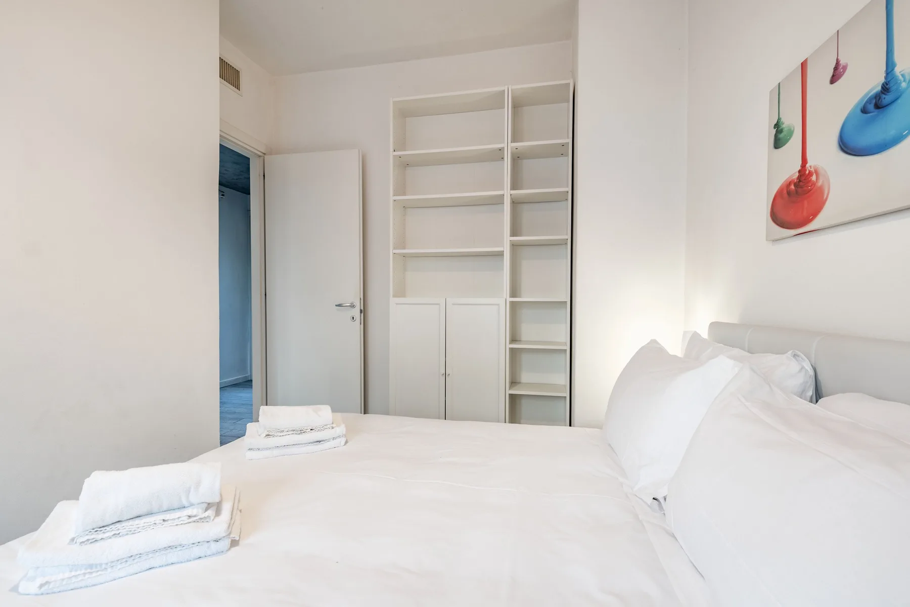 Un dormitorio luminoso con ropa de cama blanca y estantes empotrados junto a la puerta abierta.