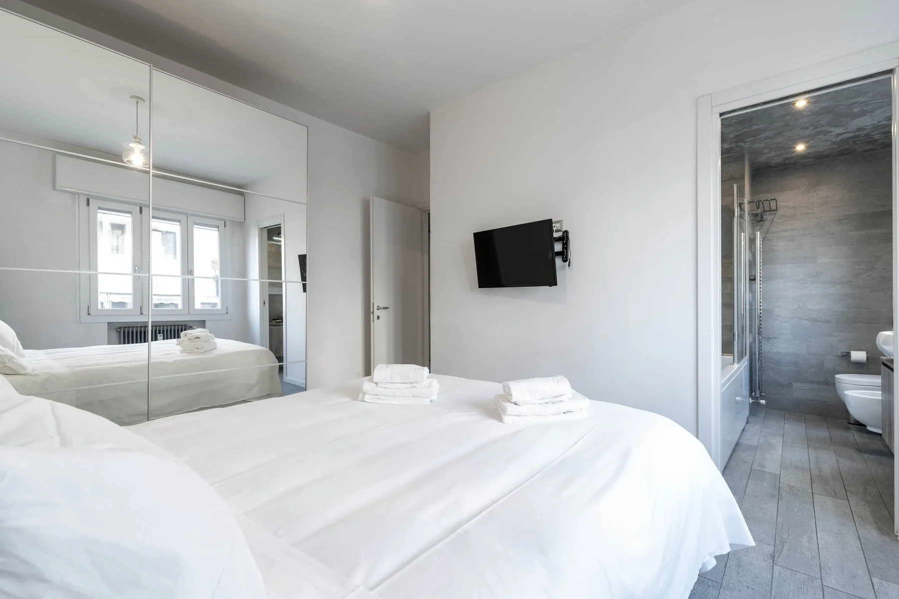 Un dormitorio luminoso con una cama bien hecha y una puerta abierta al baño.