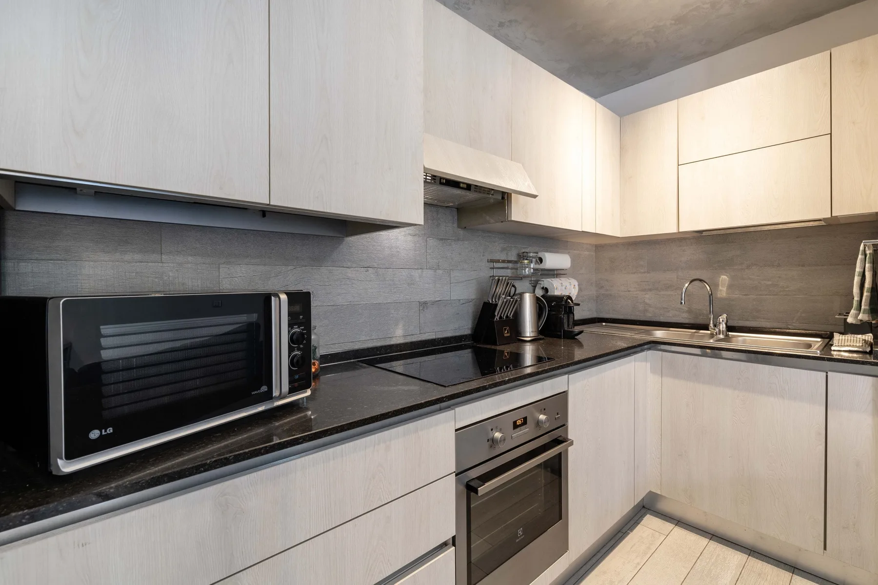 Una cocina moderna con gabinetes claros, encimeras oscuras y electrodomésticos integrados.