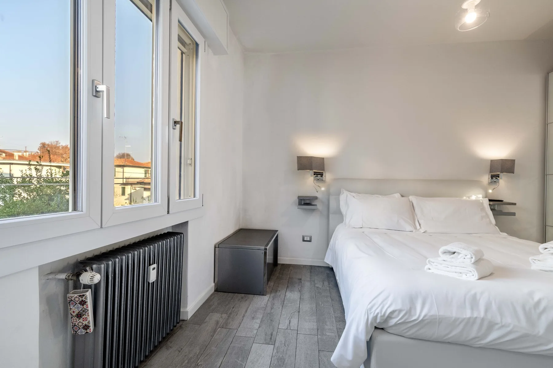 Un dormitorio luminoso con una cama blanca junto a grandes ventanas.