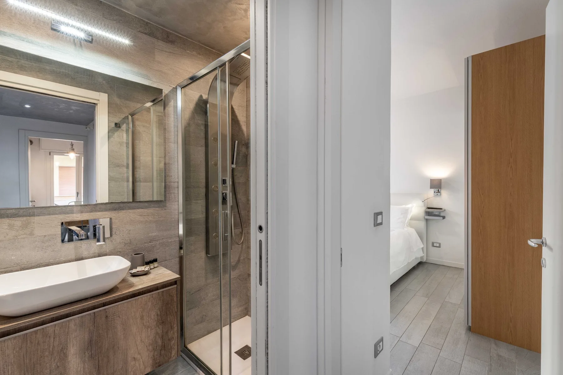 Un baño con un espejo grande y una ducha de vidrio junto a un dormitorio.