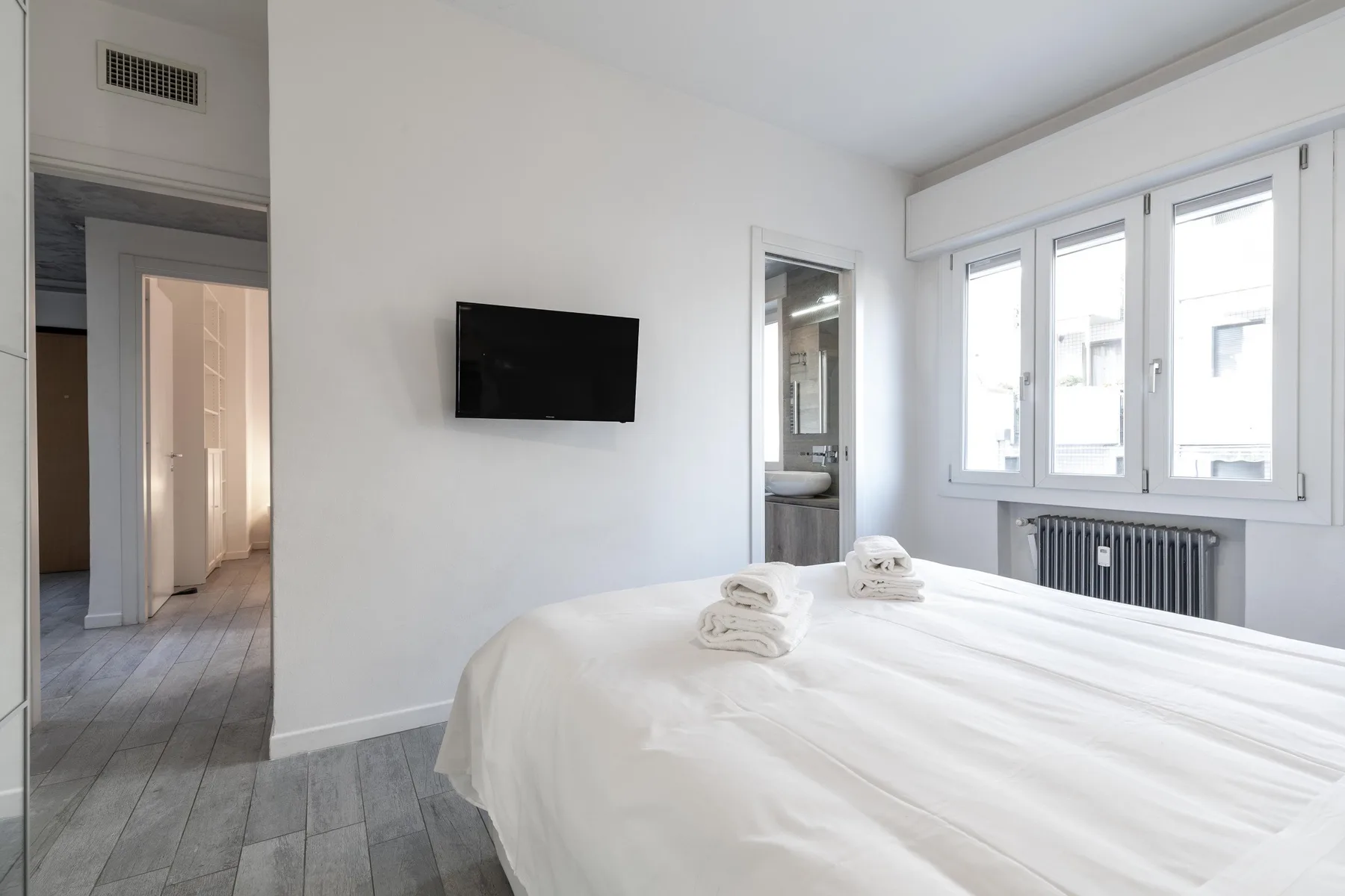 Un dormitorio luminoso con una cama bien hecha y ventanas a lo largo de una pared.