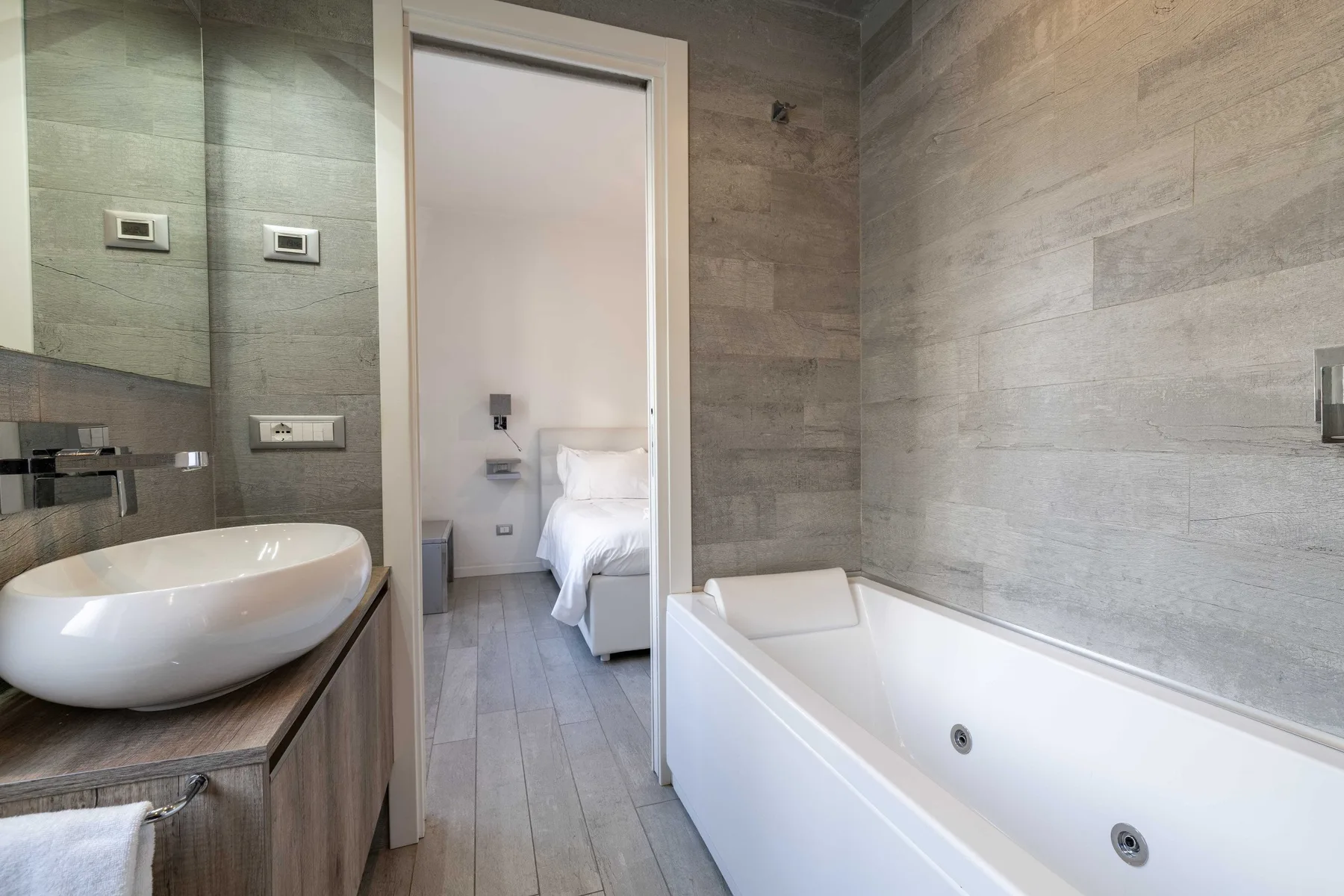Un baño alicatado con bañera y una puerta abierta hacia un dormitorio.