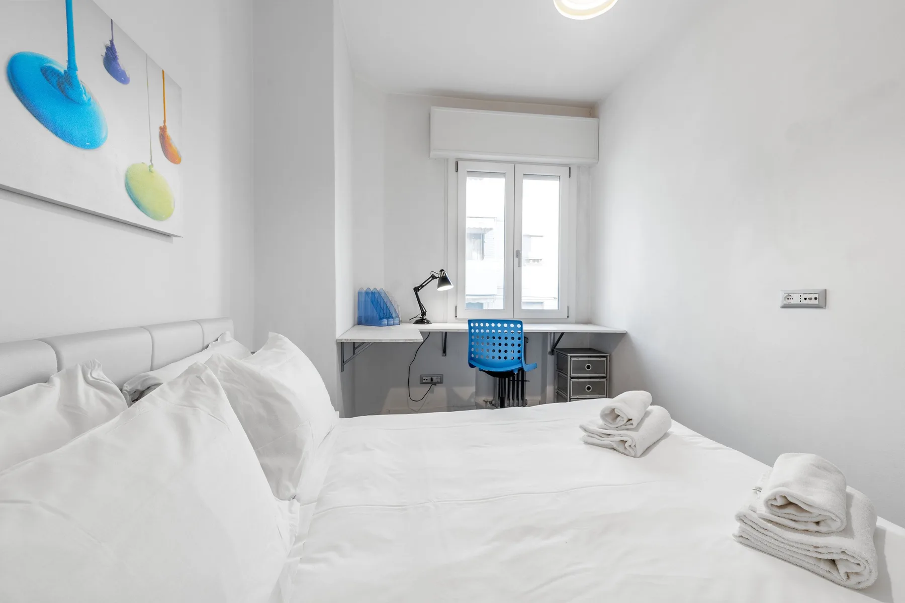 Un dormitorio luminoso con una cama y un escritorio bajo la ventana.